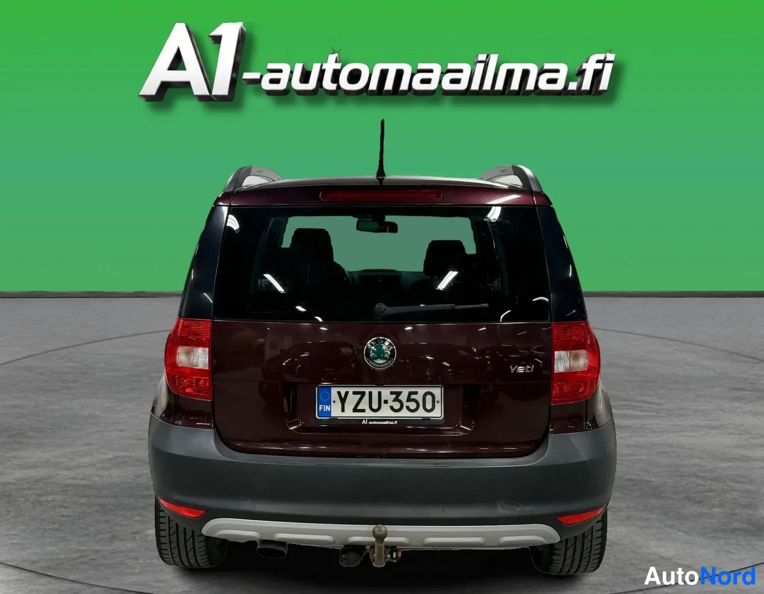 Takaa: Tummanpunaisen Skoda Yetin takanäkymä: takavaloja, -rekisterikilpi ja vetoaisa näkyvät vihreää taustaa vasten.