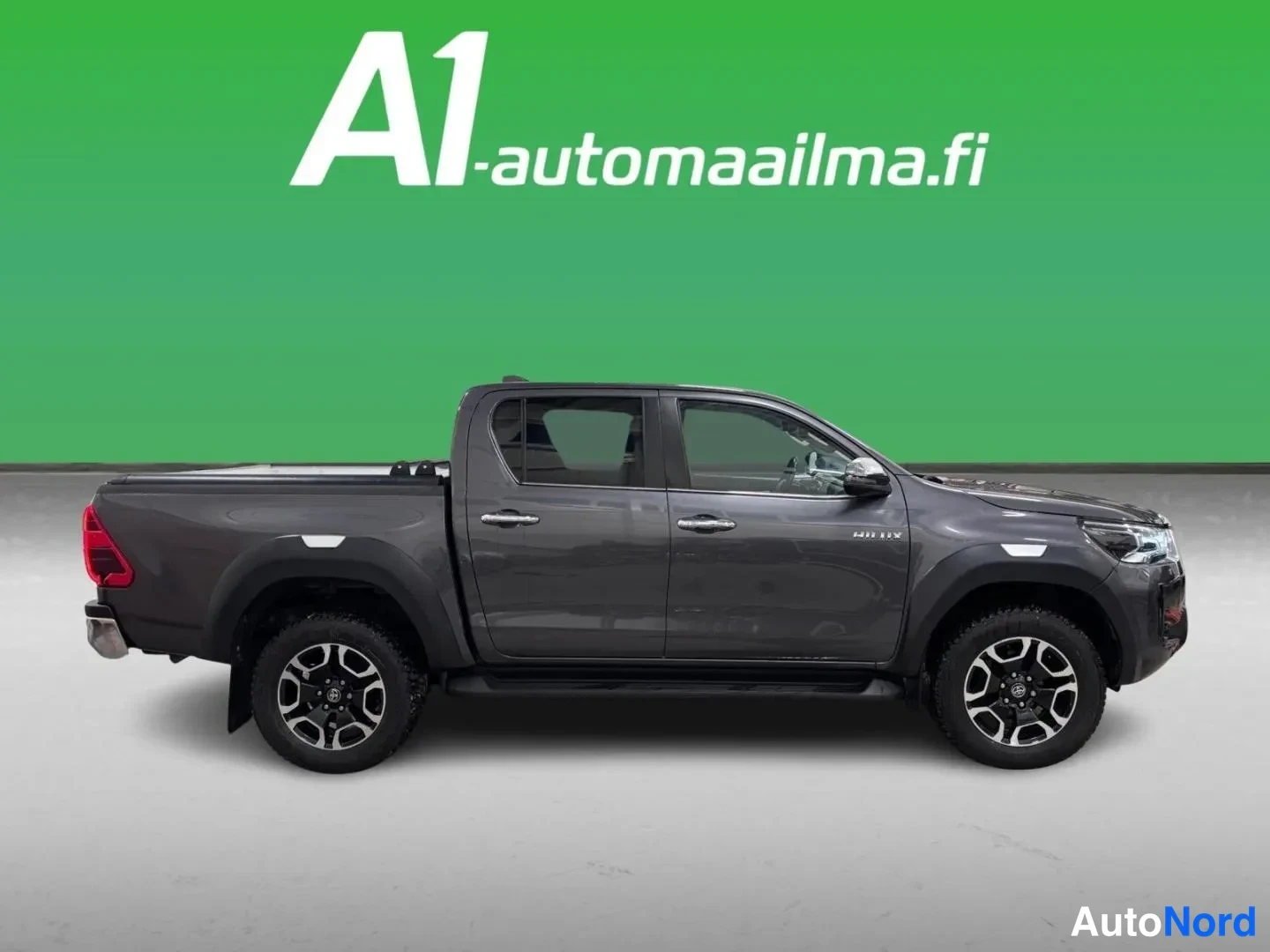 Etuviisto, nokka oikealle: Hilux Double Cab -lavallinen tummanharmaa lava-auto profiilista oikealle, mustat taittovanteet ja sivukaiteet näkyvissä.