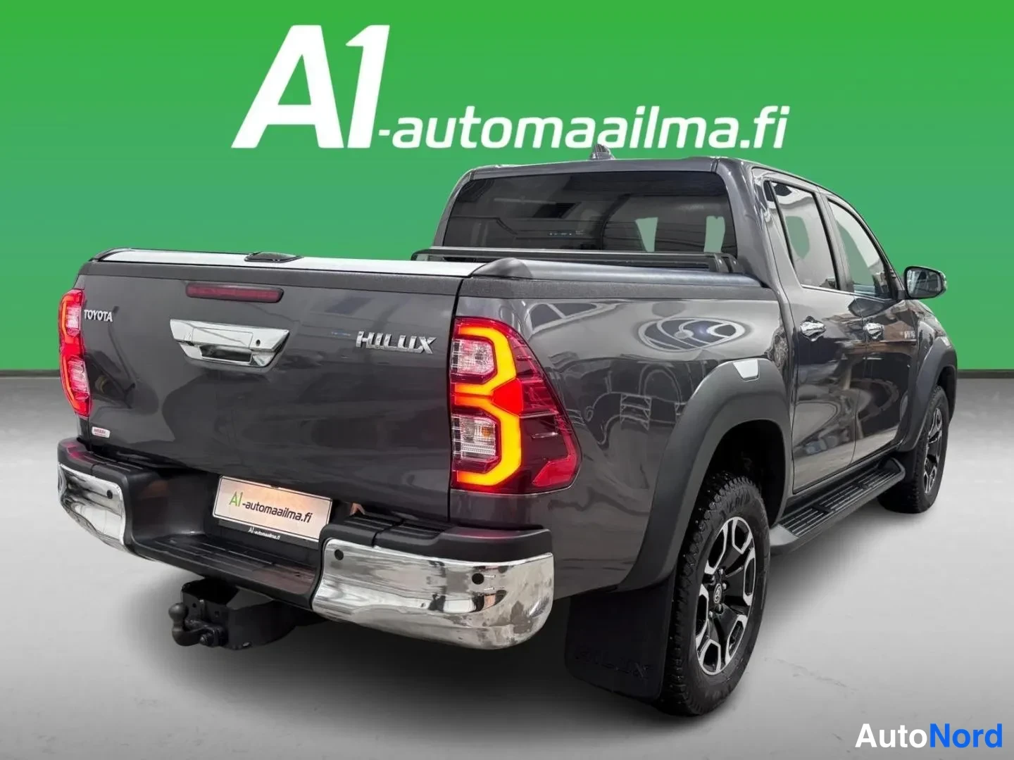 Takaviisto: Tummanharmaan Toyota Hilux -laccapickupin takakulma, takavalo palaa, kirjaimet TOYOTA ja HILUX takapaneelissa.