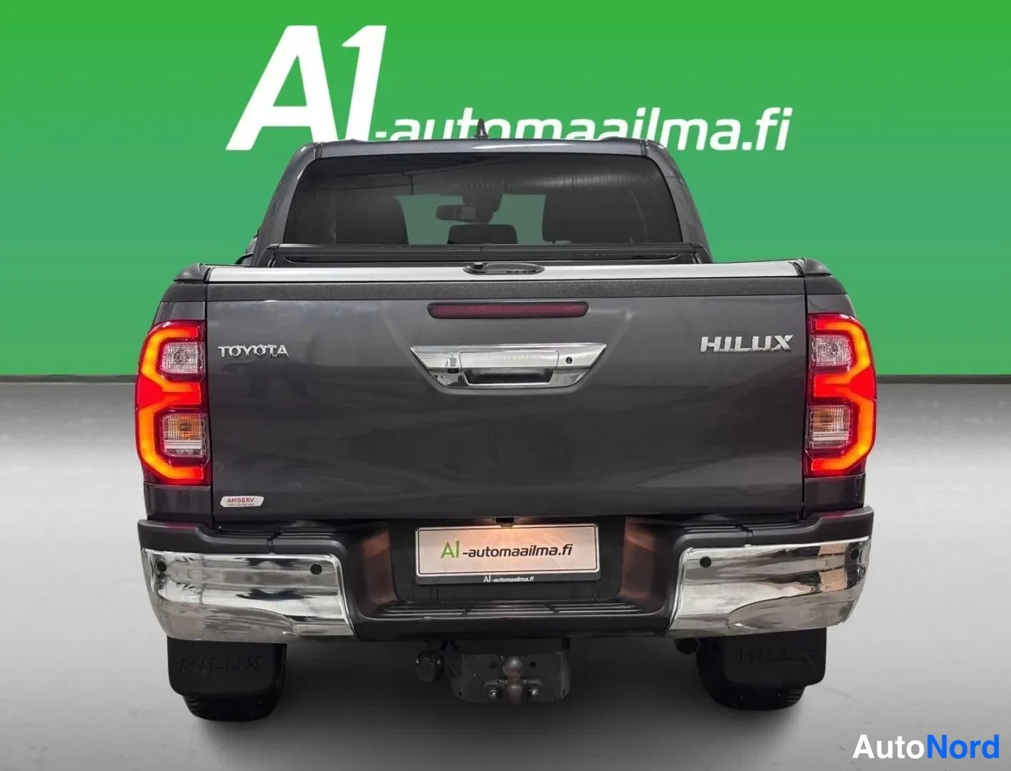 Takaa: Auton takaosa suoraan takaa: tummanharmaa Toyota Hilux -maastokuorma-auto, HILUX-teksti ja TOYOTA-merkki kannessa, kannen päällä suojakansi, kromipuskuri ja vet