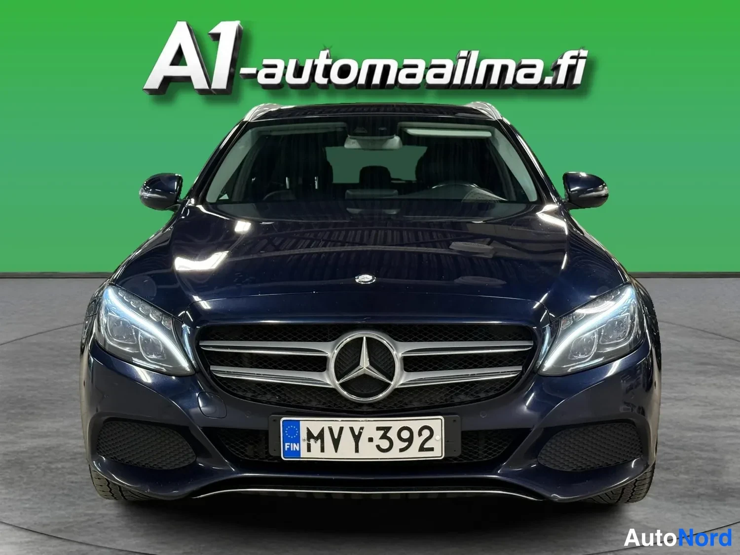 Edestä: Tummansininen Mercedes-Benz suoraan edestä; Mercedes-tähti etusäleikössä, rekisterikilpi.