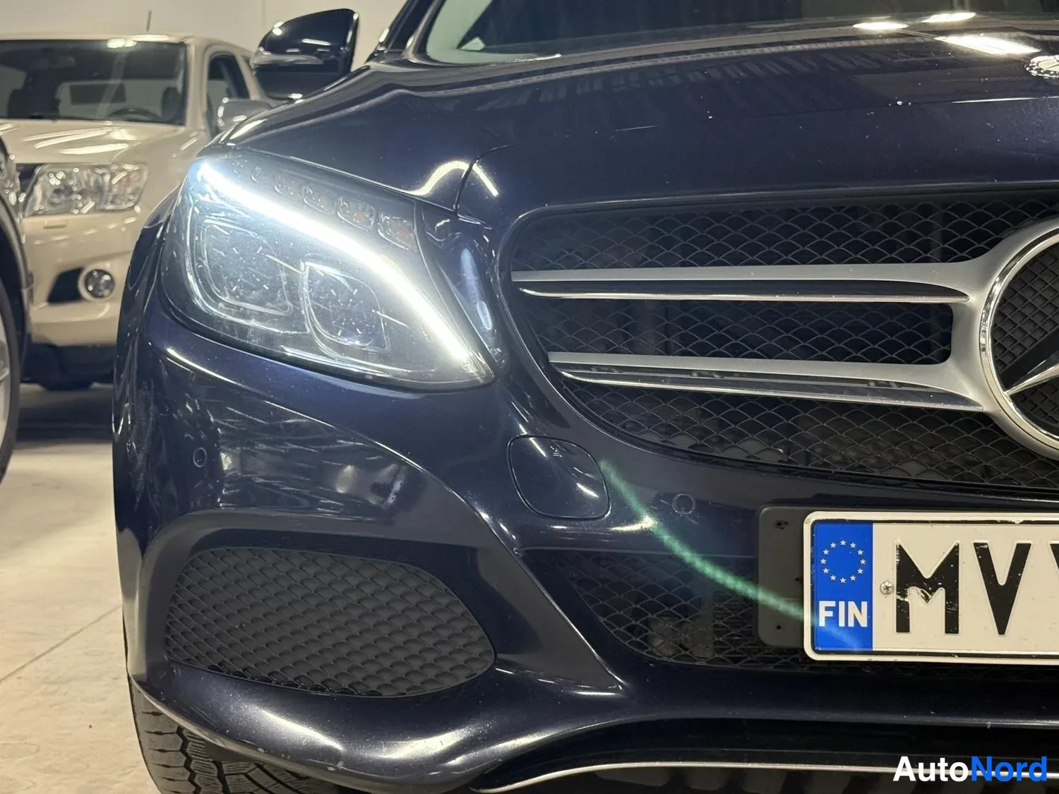 Edestä: Mercedes-Benzin etupää lähikuvassa: tummasininen konepelti ja etupuskuri, LED-etuvalot päällä, DIAMOND-ristikkojäminen etusäleikkö tähtimerkillä ja sinivalkoine