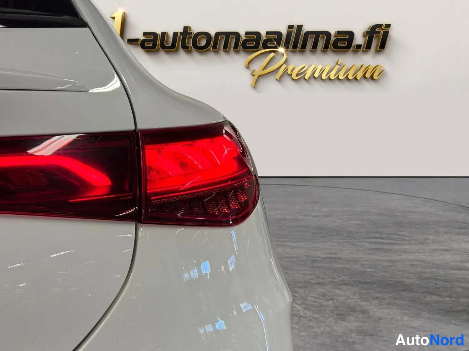 Takaa: Auton takakulma lähikuvassa, punainen takavalo ja vaalea kori, taustalla automaalilogo.