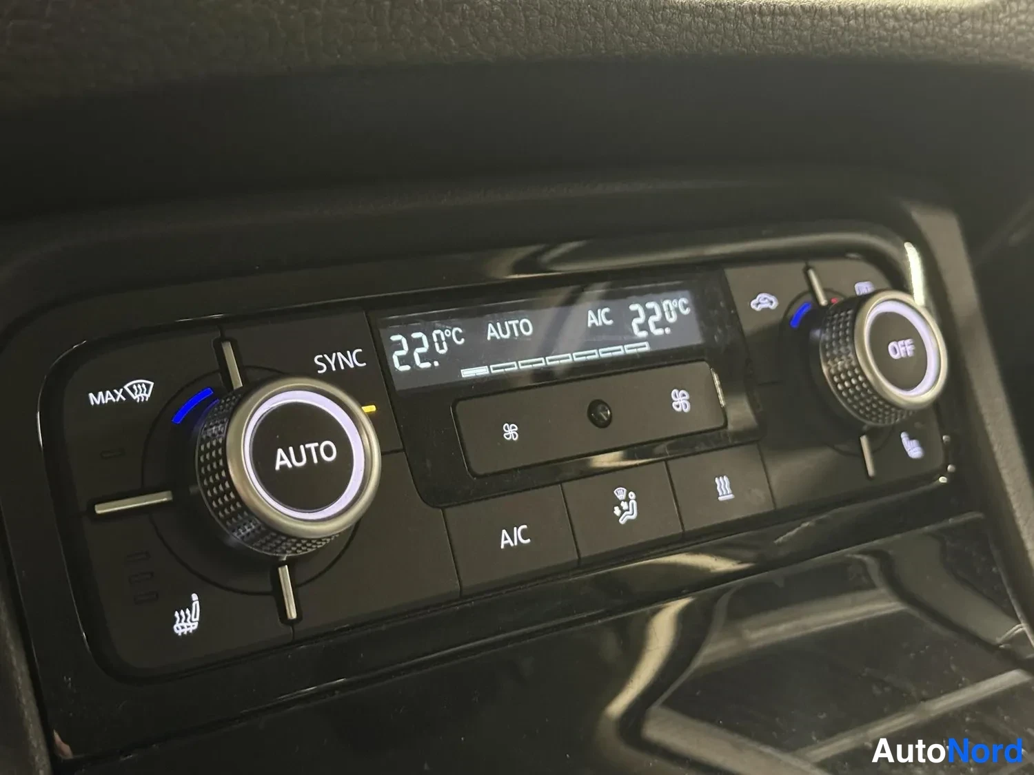 Muu: Auton sisätilan ilmastoinnin hallintapaneeli: näytöllä 22,0 °C, AUTO ja A/C -tekstit, kaksi säädinnuppia ja SYNC-merkintä.