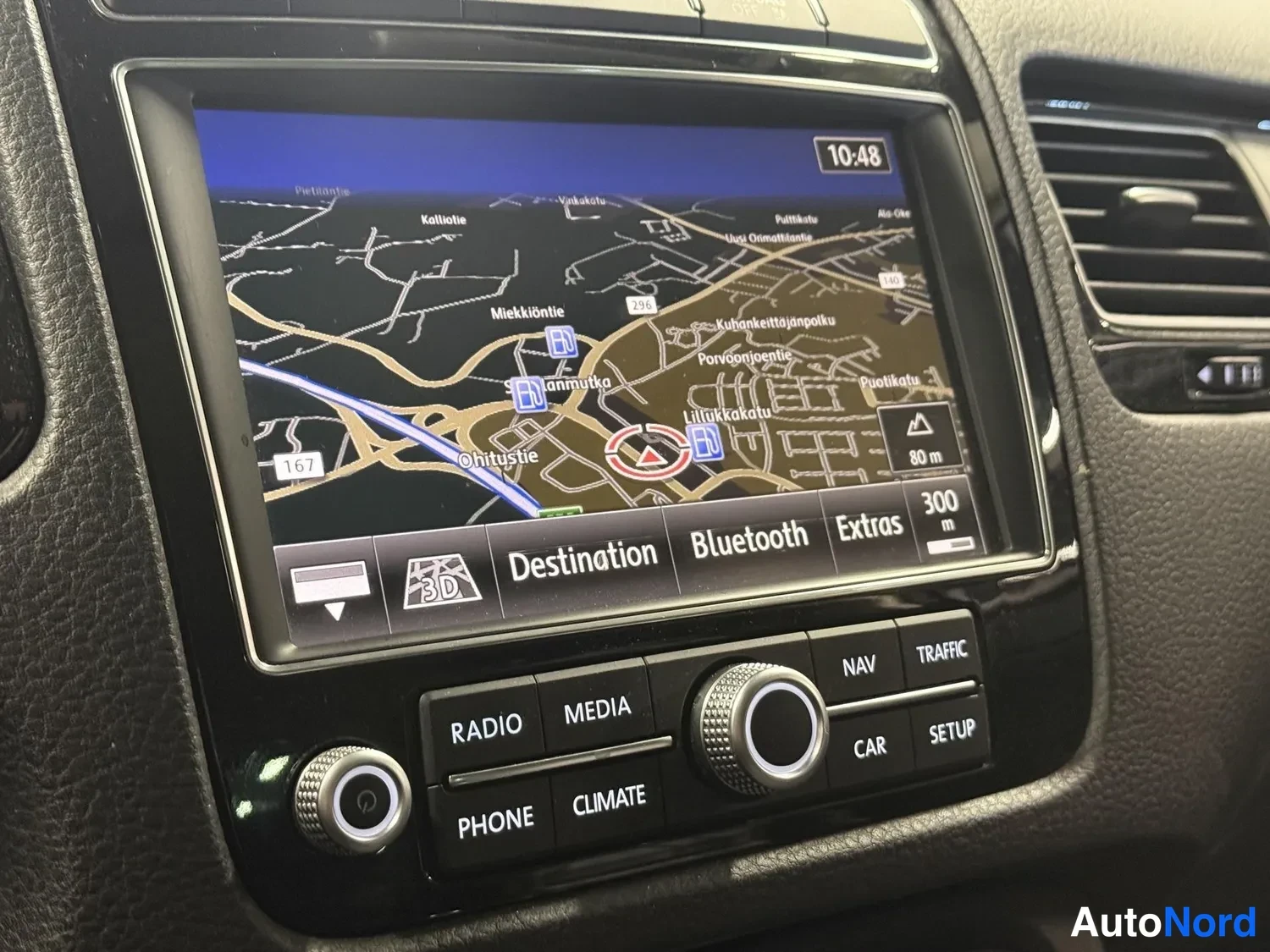 Muu: Volkswagenin.Navigation näkymä konsolin ruudulla: kartta, kellonaika 10:48 ja painikkeet Radio, Media, Phone, Climate, Nav, Traffic, Car, Setup.