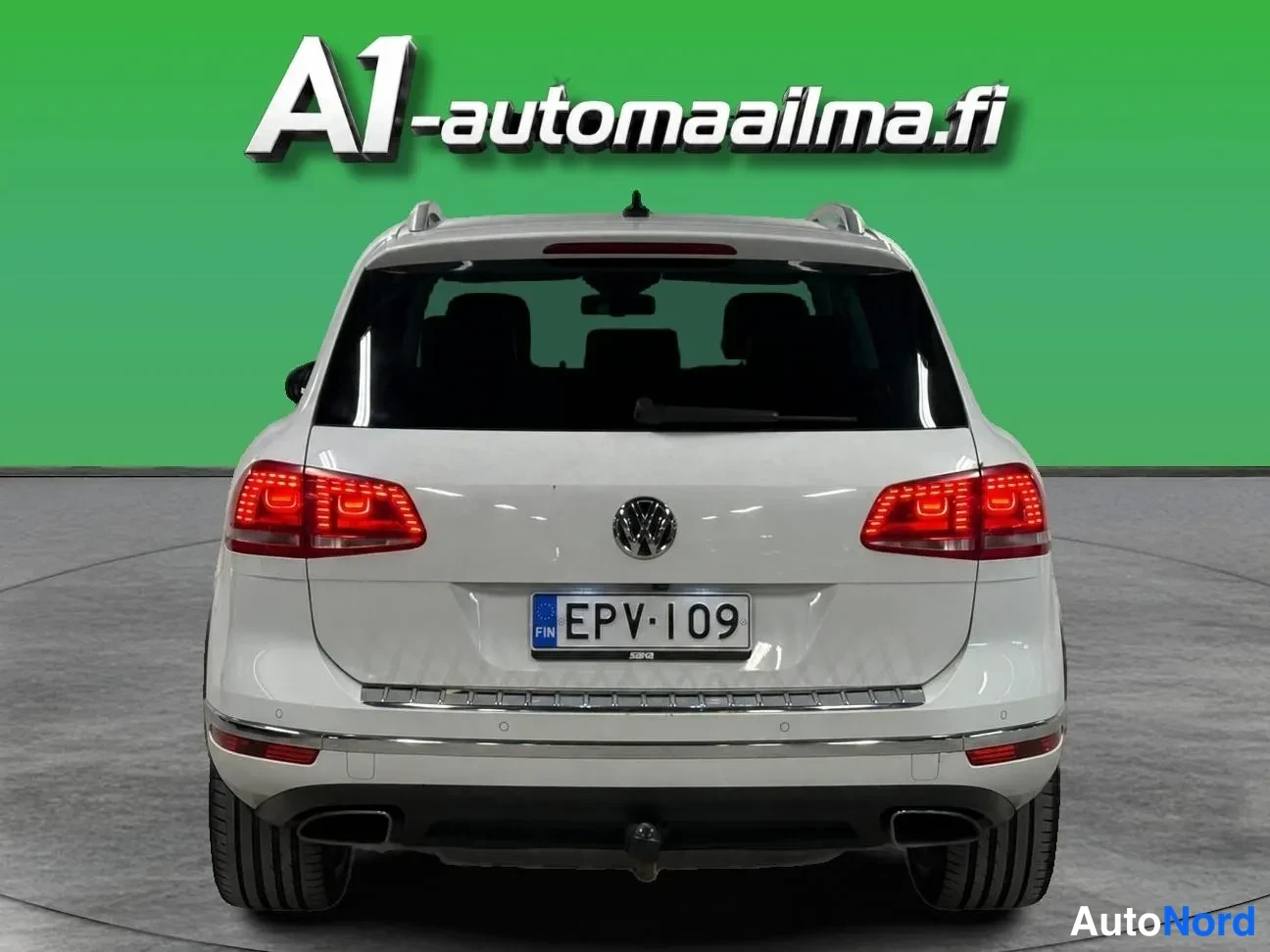 Takaa: Auton takanäkymä: valkoinen Volkswagen, punaiset takavalot, rekisteritunnus, kattotelineet ja kaksiosaiset pakoputket.