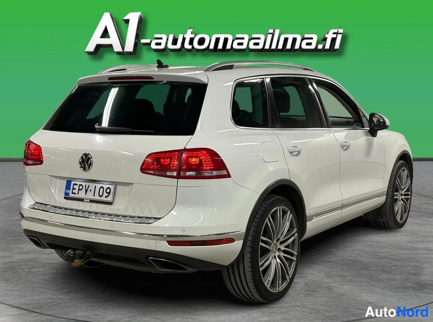 Takaviisto: Auton takaa sivulta kuvattu näkymä: valkoinen Volkswagen, mustat ikkunat, kattotelineet ja hopeametallivanteet.