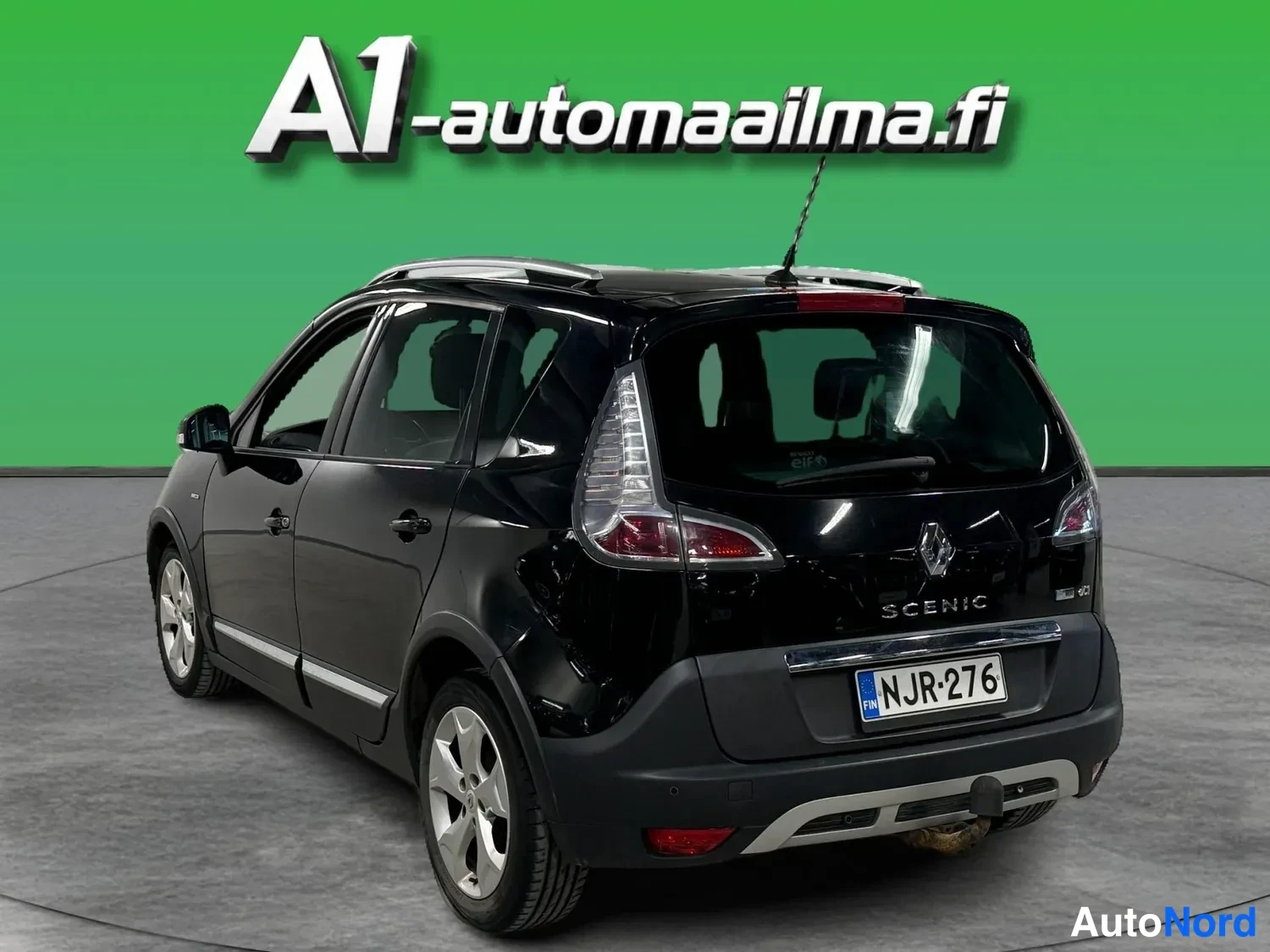 Takaviisto: Mustan Renault Scenicin takakulmanäkymä, takavalojen, peräluukun ja rekisterikilven näkyessä.