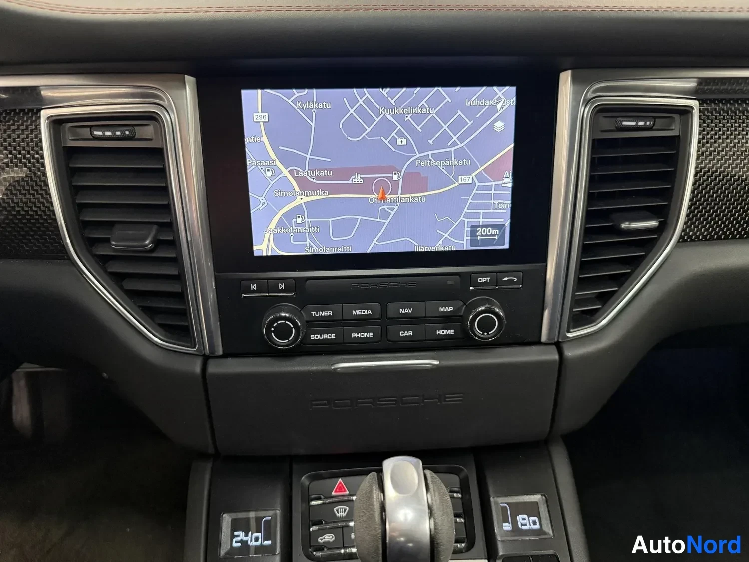 Muu: Porsche-kojetaulun keskusnäyttö näyttää karttaa navigoinnista Helsingin alueella; alapuolella TUNER-, MEDIA-, NAV-, MAP-, SOURCE-, PHONE-, CAR- ja HOME-painikke