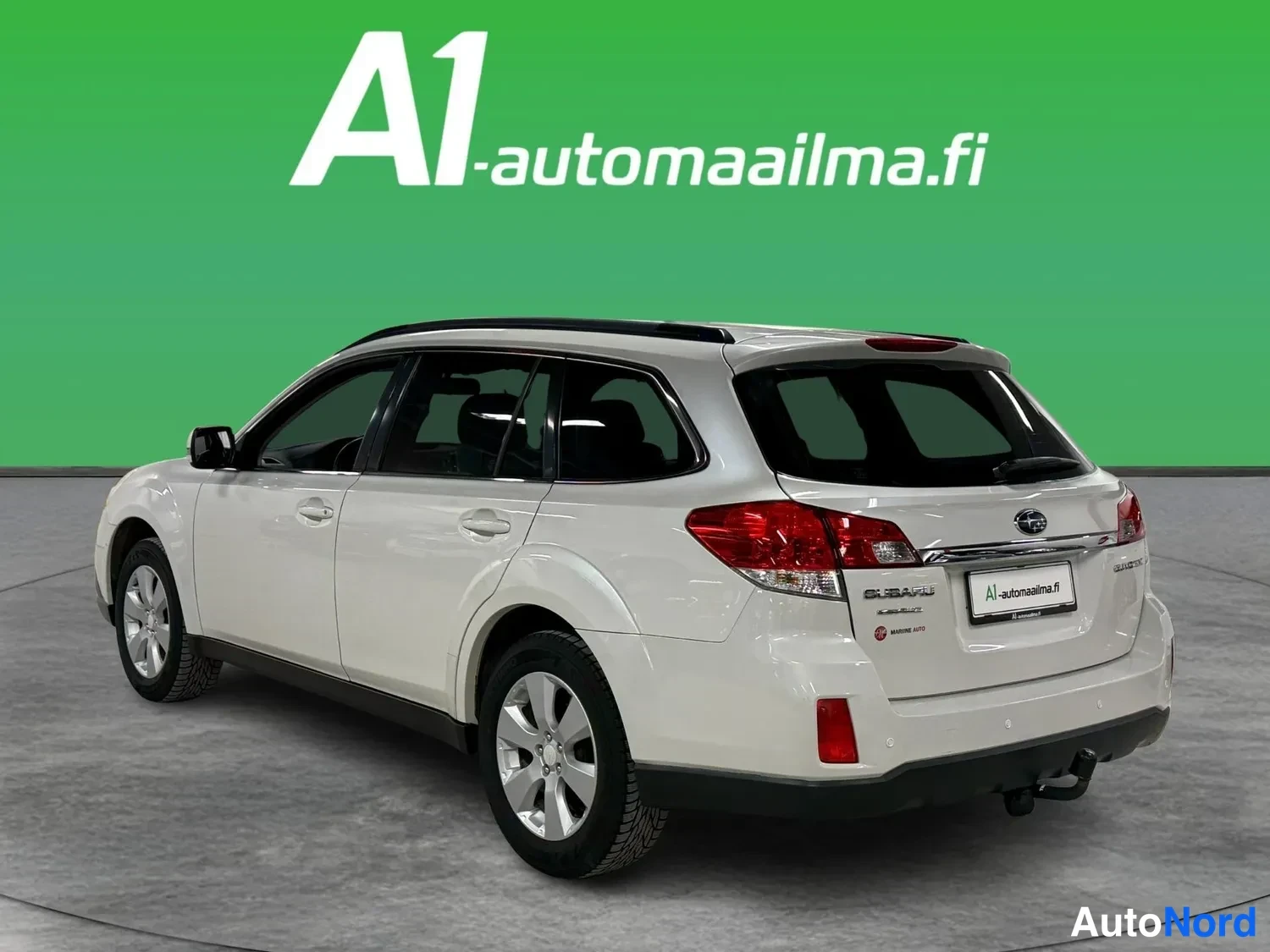 Takaviisto: Subaru Outback -farmari takaosaltaan ja oikean sivulleen näkyvästi valokuvattu, valkoinen kori, takavaloissa neljä pyöreää elementtiä, punaiset takavalot, musta