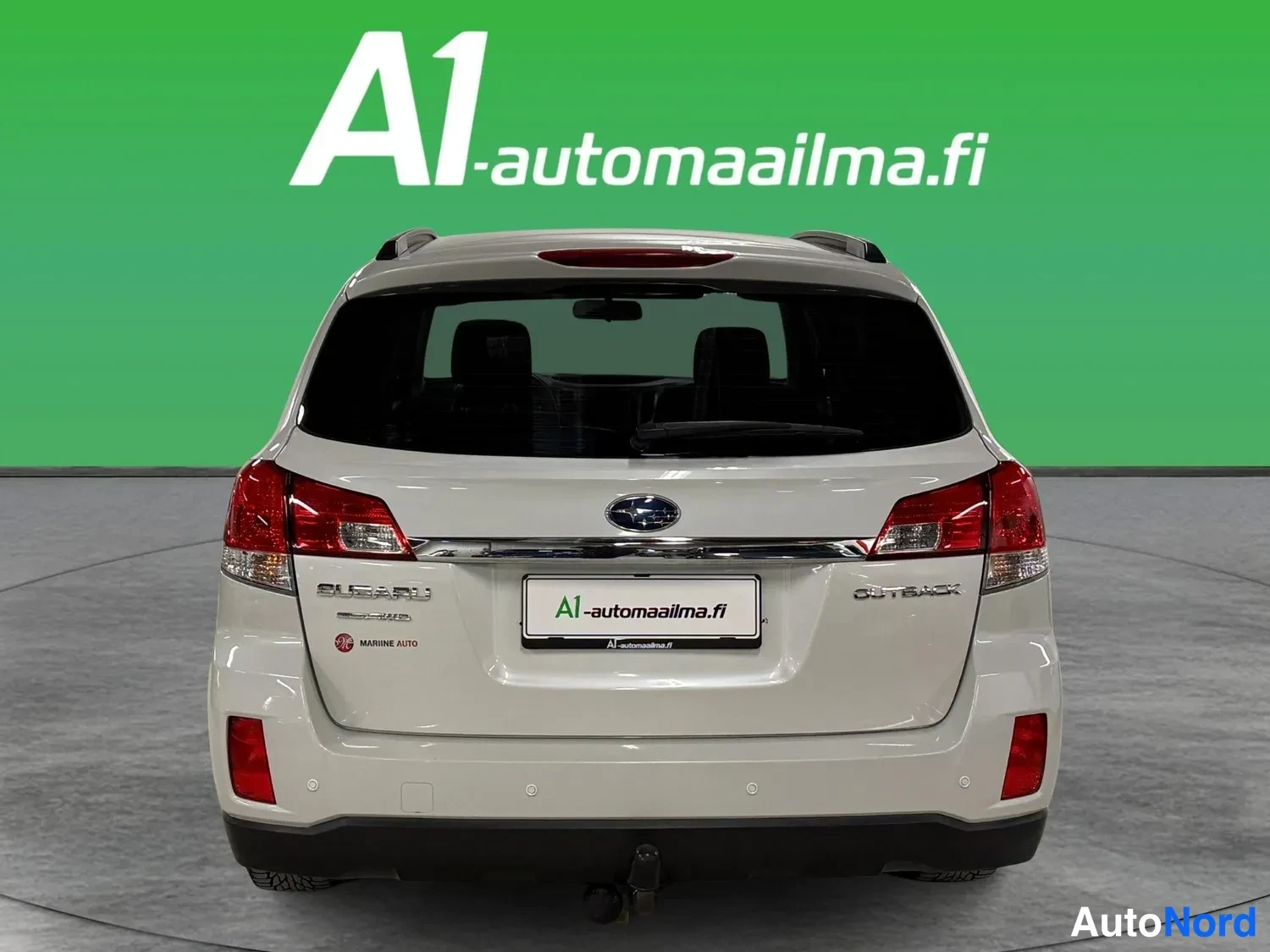 Takaa: Auton takaosa suoraan takaa: valkoinen farmariauto, Subaru-merkintä ja A1-automaailma.fi-kilpi takaluukussa, punaiset takavalot, irrotettava vetokoukku.
