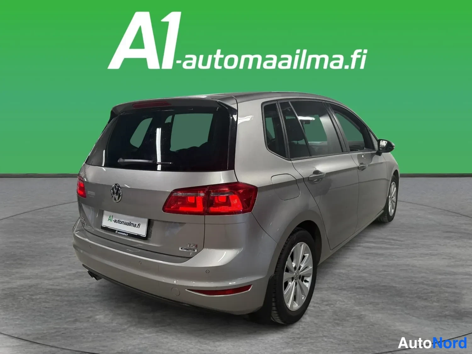Takaviisto: Volkswagen Golf Sportsvan -farmarin takaosan kolmannesvasen näkymä: hopeanharmaa koripaneeli, takaovat, takavalojen punaiset yksiköt ja A1-automaailman mainosta