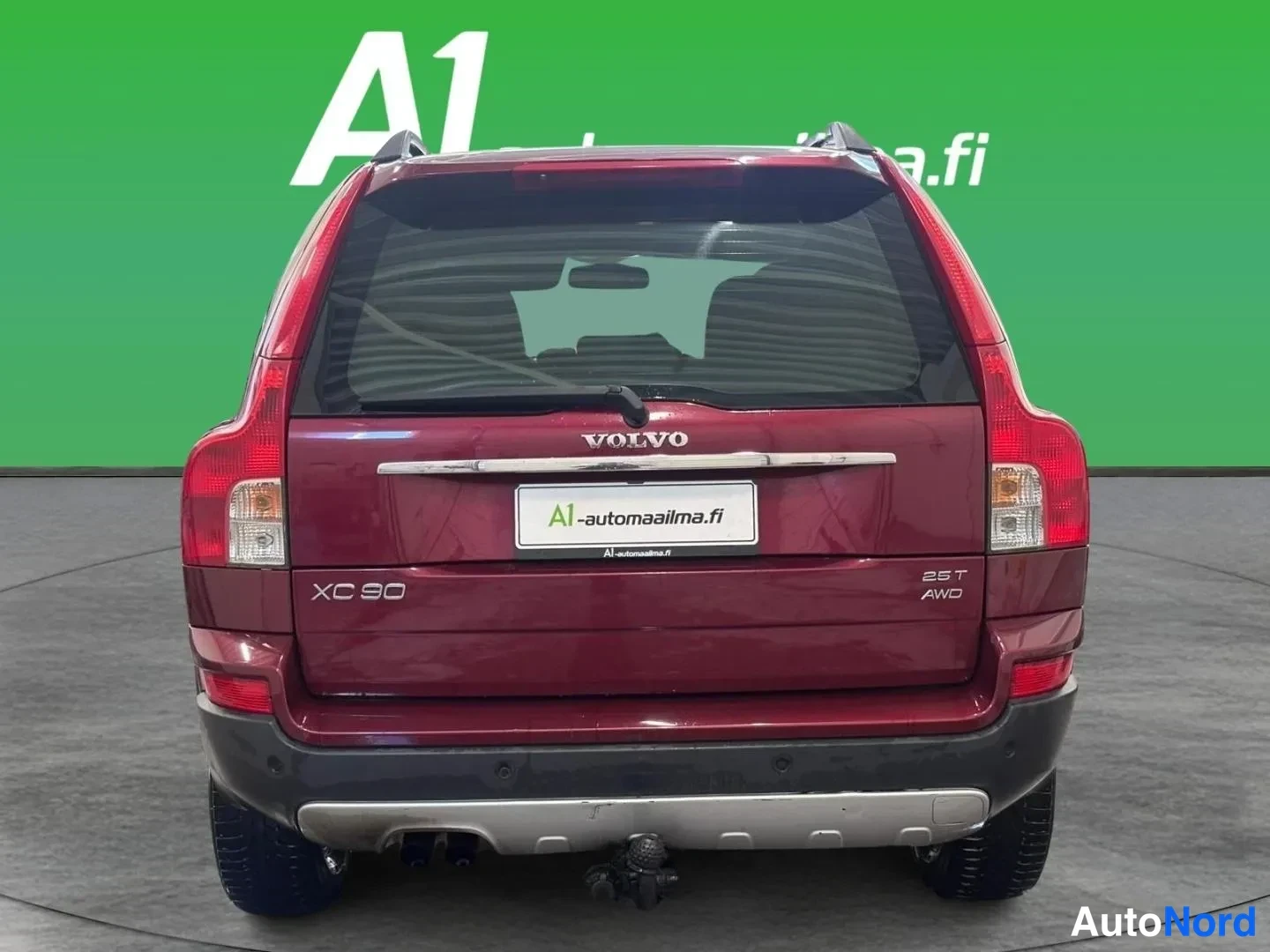 Takaa: Takaapäin kuvattu tummanpunainen Volvo XC90, takavalot, VOLVO-merkintä, XC90- ja 2.5T AWD-embleemit sekä vetokoukku näkyvissä.