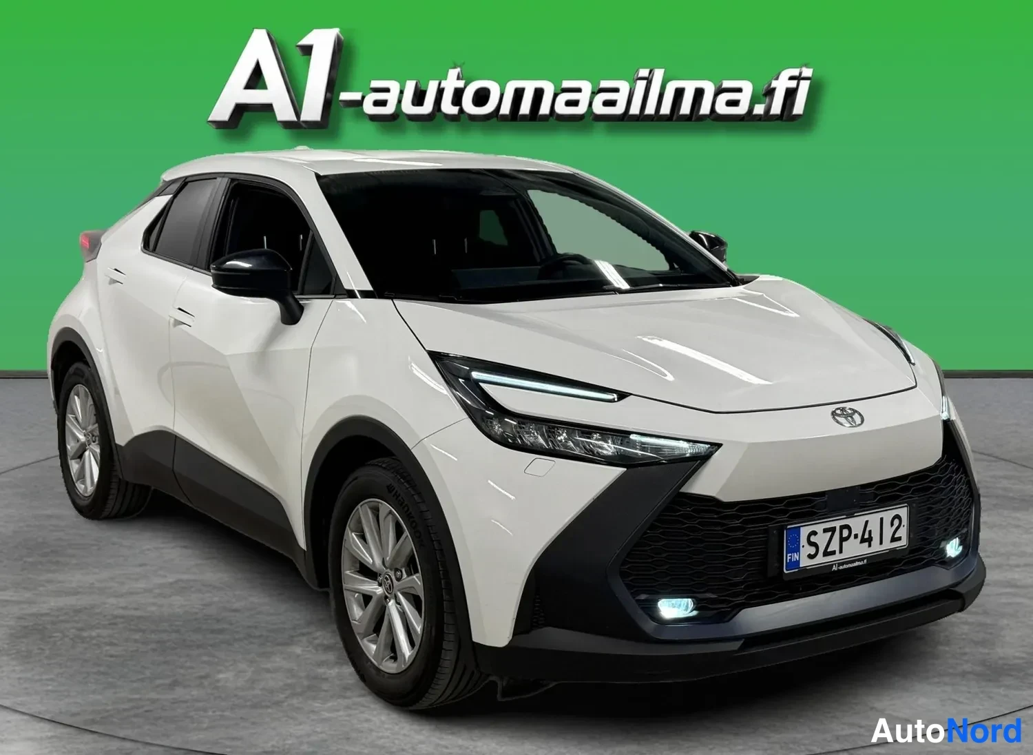 Etuviisto, nokka oikealle: Toyotan etukolmasosa: valkoinen crossover-mallinen auto, rekisteritunnus, musta etusäleikkö ja LED-etuvalot vihreää taustaa vasten.
