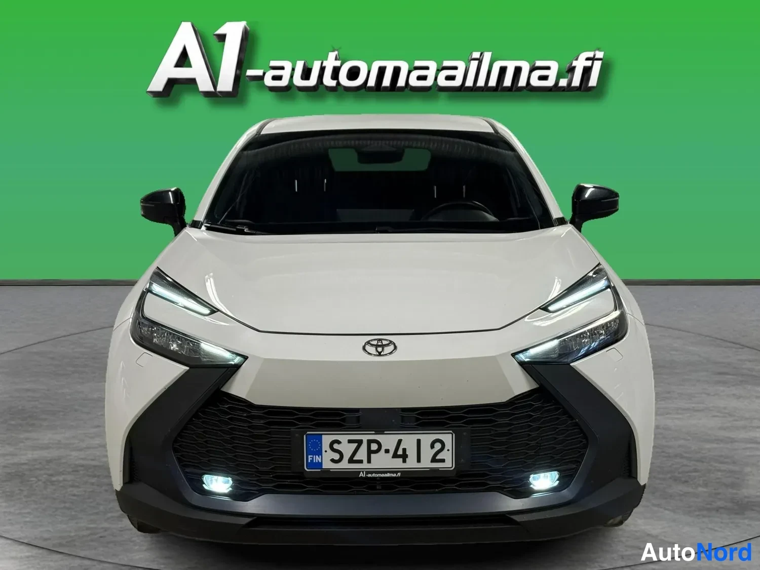 Edestä: Toyota suoraan edestäpäin: valkoinen kori, musta etusäleikkö, rekisteritunnus, ohuet LED-etuvalot.
