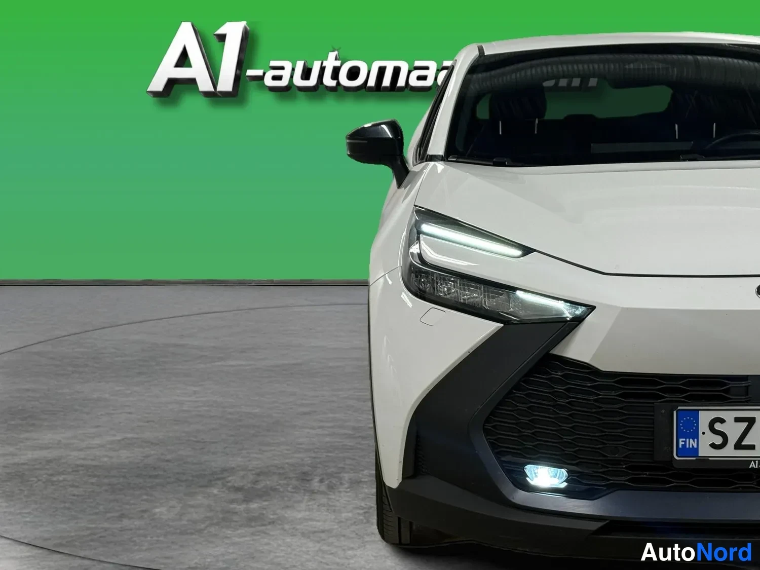 Edestä: Valkoisen Toyota C-HR:n etupää lähikuvassa; ohut LED-päiväajovalo, tumma etusäleikkö ja rekisterikilven alkua SZ näkyvät.