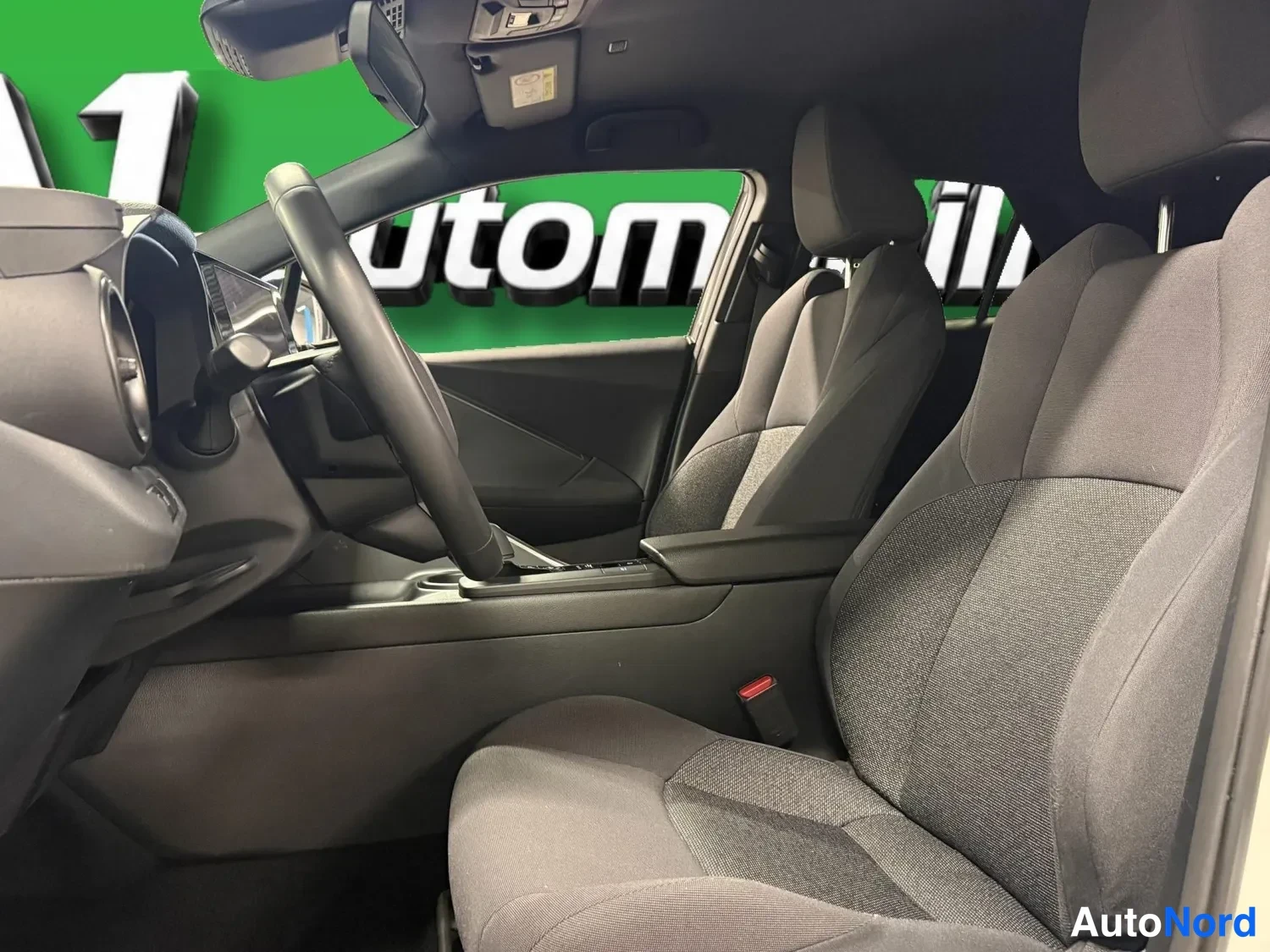 Muu: Sisätilakuva Toyota C-HR -autosta: kuljettajan istuin ja ohjauspyörä etualalla, tummaa kankaita verhoilu, keskiarmarelli ja takapenkin istuimet näkyvät.