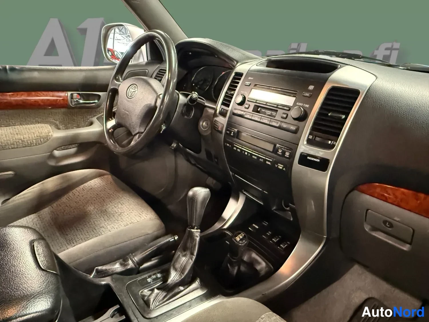 Edestä: Ohjaamo lähikuvana: Toyota-ohjauspyörä, kojelaudan radio ja ilmastointiautomaatti, automaattivaihteen vaihdevipu, alavaihdevipu ja keskikonsolin kytkimet.