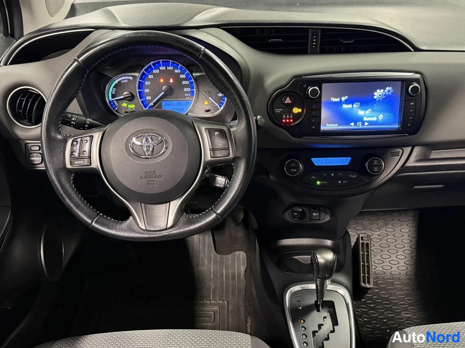 Muu: Kojelaudan kuva kuljettajan puolelta: Toyota-ohjauspyörä, hybridimittaristo, kosketusnäyttö, automaattivaihteisto ja ilmastointilaitteet.