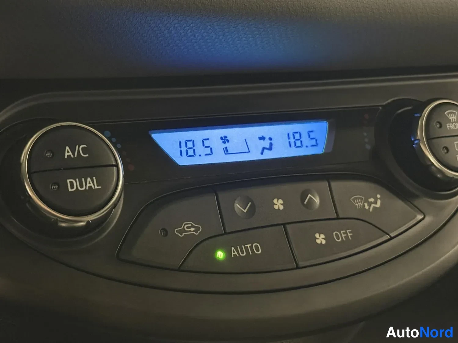 Muu: Lähikuva ilmastointipaneelista: A/C- ja DUAL-napit, näytössä 18,5 molemmilla puolilla sekä AUTO- ja OFF-napit.