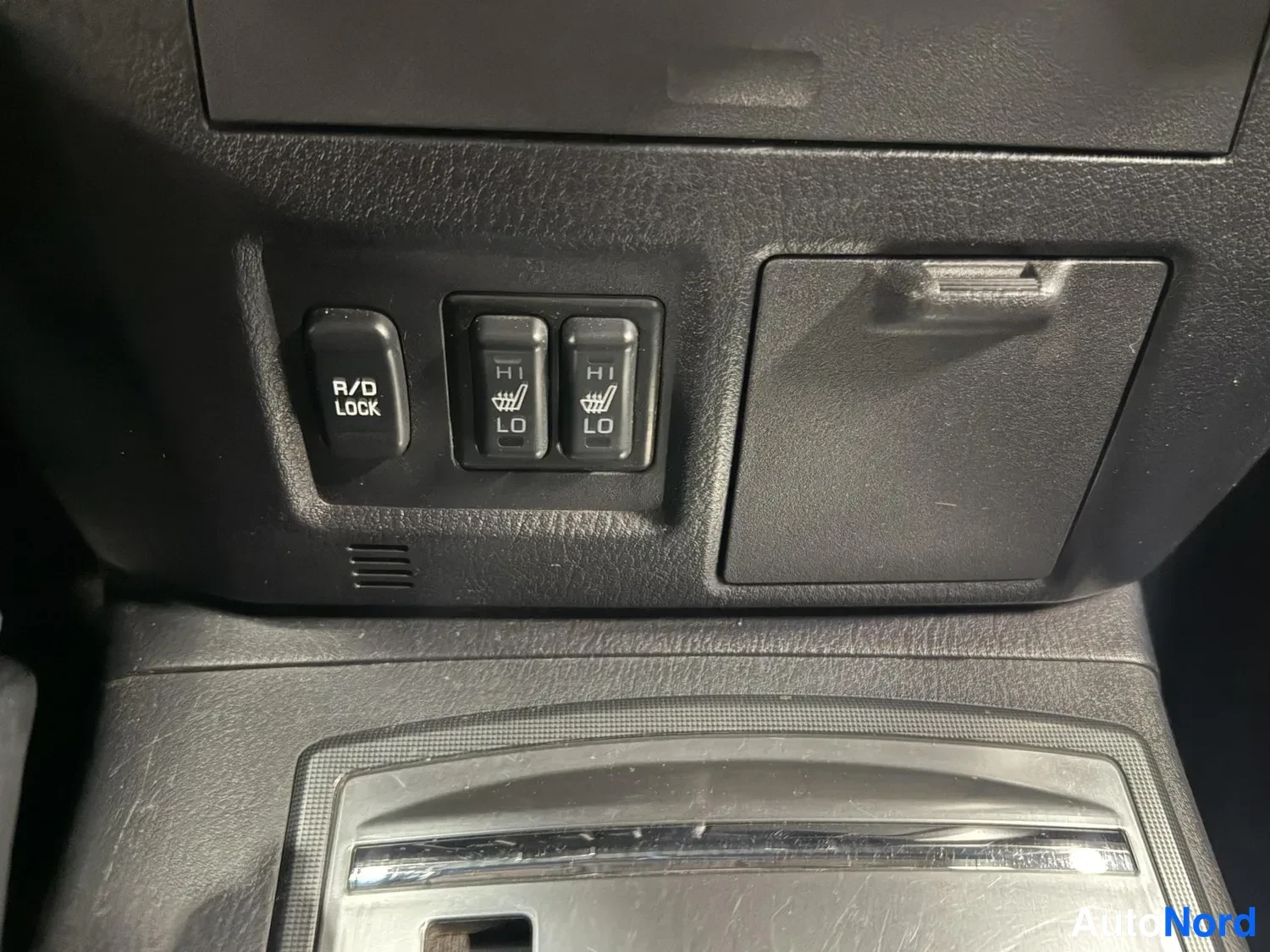 Edestä: Konsolin kytkimet: R/D LOCK -kytkin sekä kaksi lämmitettävien istuinten kytkintä merkinnöillä HI/LO.