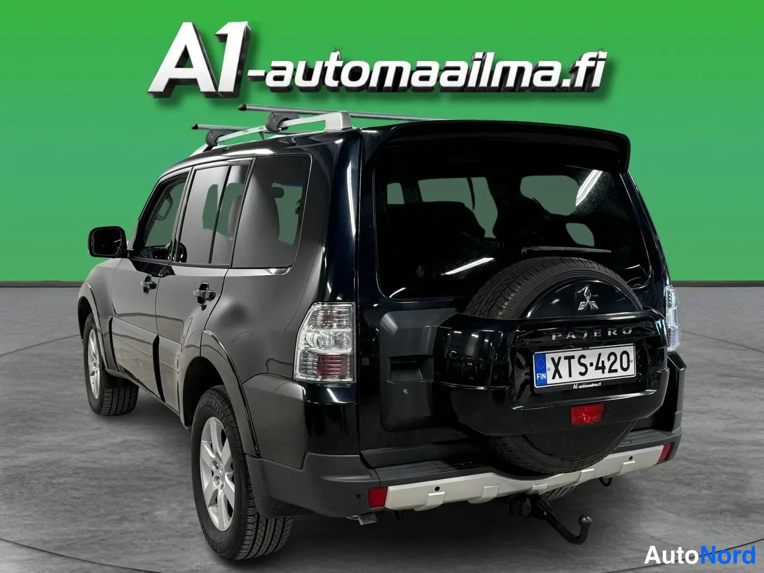 Takaviisto: Musta Mitsubishi Pajero kolmivartalokulmassa takaa vasemmalta, rekisteritunnus, varaoppa takaluukilla, PAJERO-teksti ja veto koukku takapuskurissa.