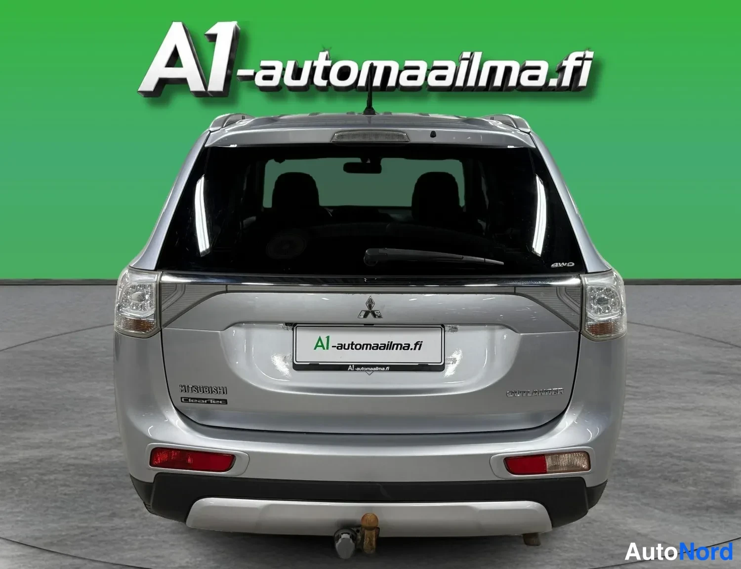 Takaa: Hopeanvärinen auton takapää suoraan takaa kuvattuna, Mitsubishi-merkki ja takavalojen välinen kromilista, vetokoukku takapuskurissa.