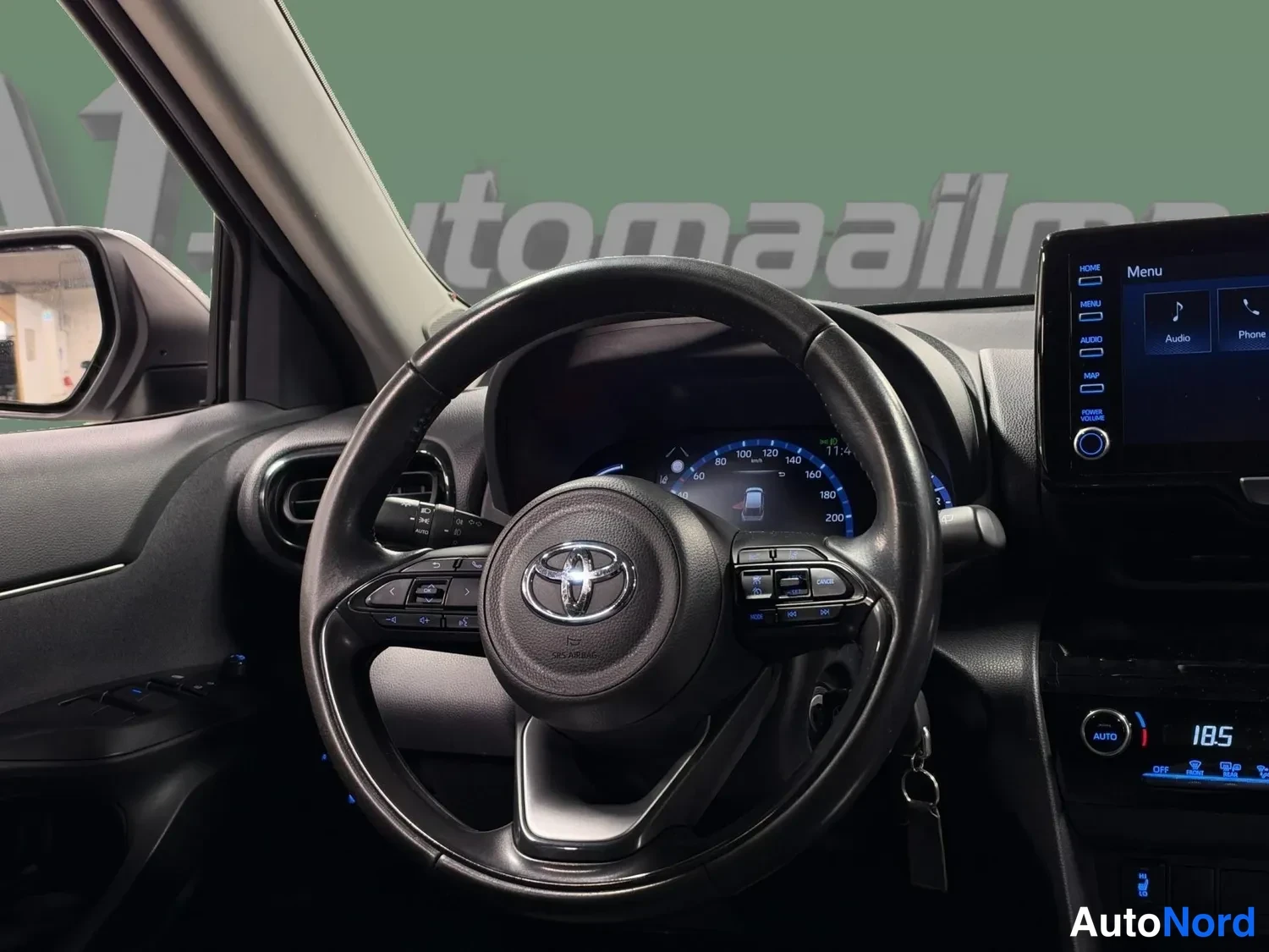 Muu: Ohjauspyörän lähikuva Toyota-merkillä, taustalla mittaristo, kosketusnäyttö ja lämpötilanäyttö 18,5 astetta.