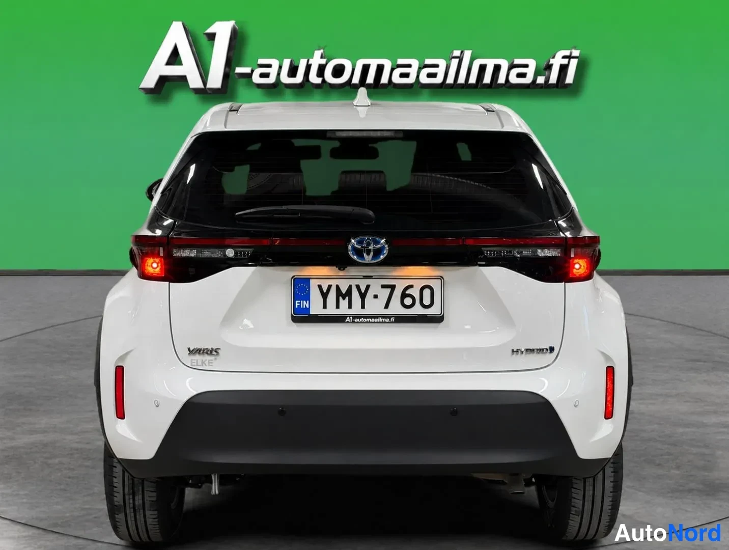 Takaa: Valkoisen Toyota Yaris Crossin suora takanäkymä; rekisteri, takavalot ja HYBRID-merkintä.