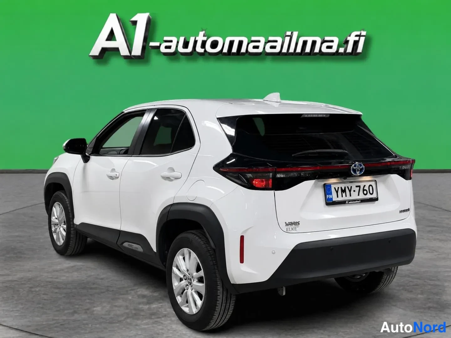 Takaviisto: Valkoisen Toyota Yaris Crossin takakulmanäyttö vasemmalta; rekisteri ja vihreä tausta.