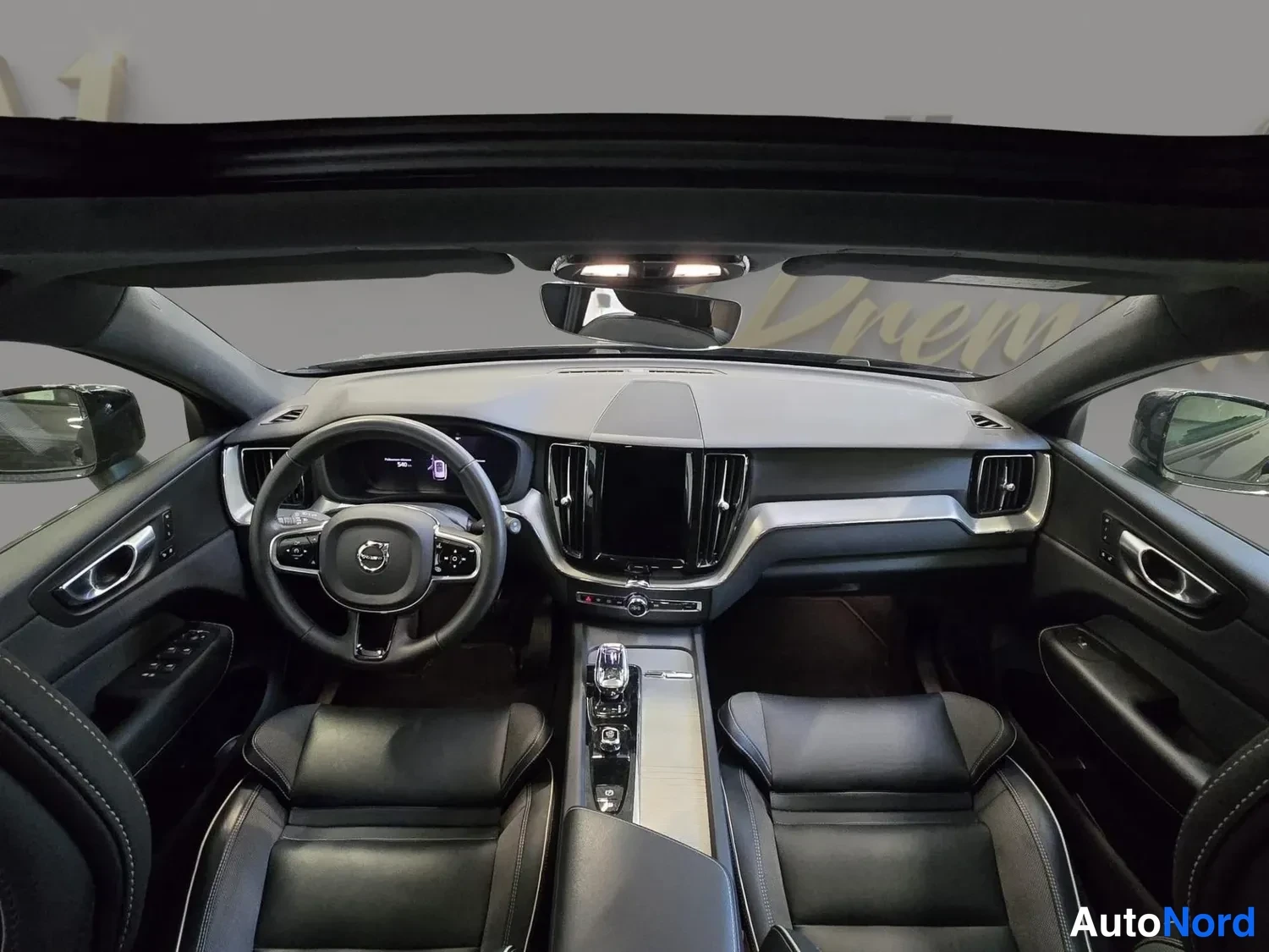 Muu: Volvo XC60:n sisätilat etuistuinten takaa kuvattuna: Volvo-logollinen ohjauspyörä, tumma kojelauta ja keskirivistön suuri kosketusnäyttö, nahkaverhoillut etuist