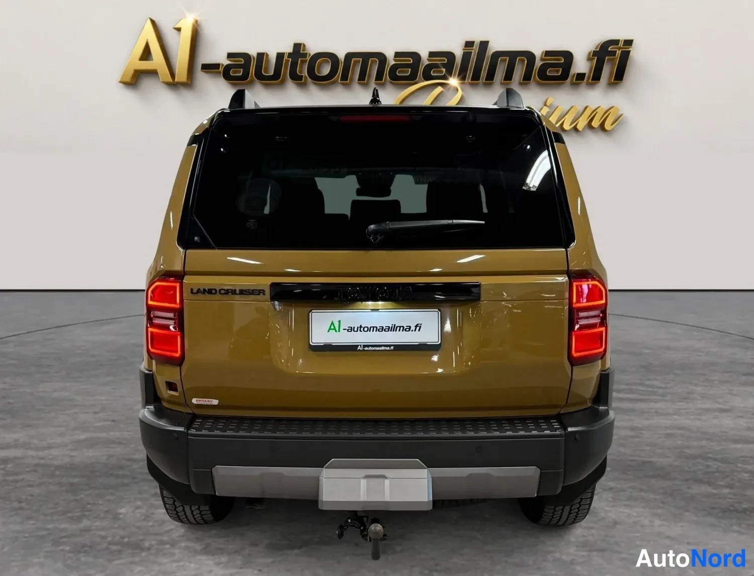 Takaa: Toyota Land Cruiserin takanäky: ruskeakultainen korirakenne, LAND CRUISER-teksti, pystysuorat punaiset takavalot, musta puskuri ja vetokoukku.