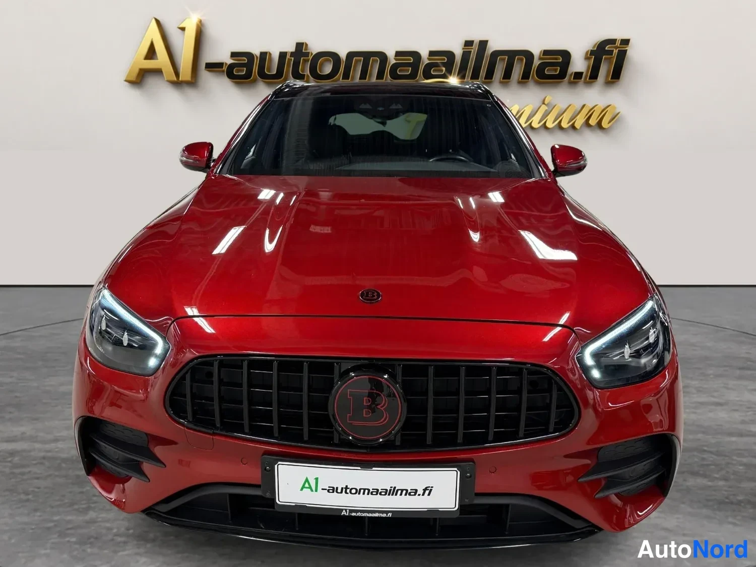 Edestä: Punaisen auton suora etukuva: musta pystysäleikköinen etusäleikkö, ohutkuvioiset ajovalot ja A1-automaailma.fi-kyltti etupuskurissa.