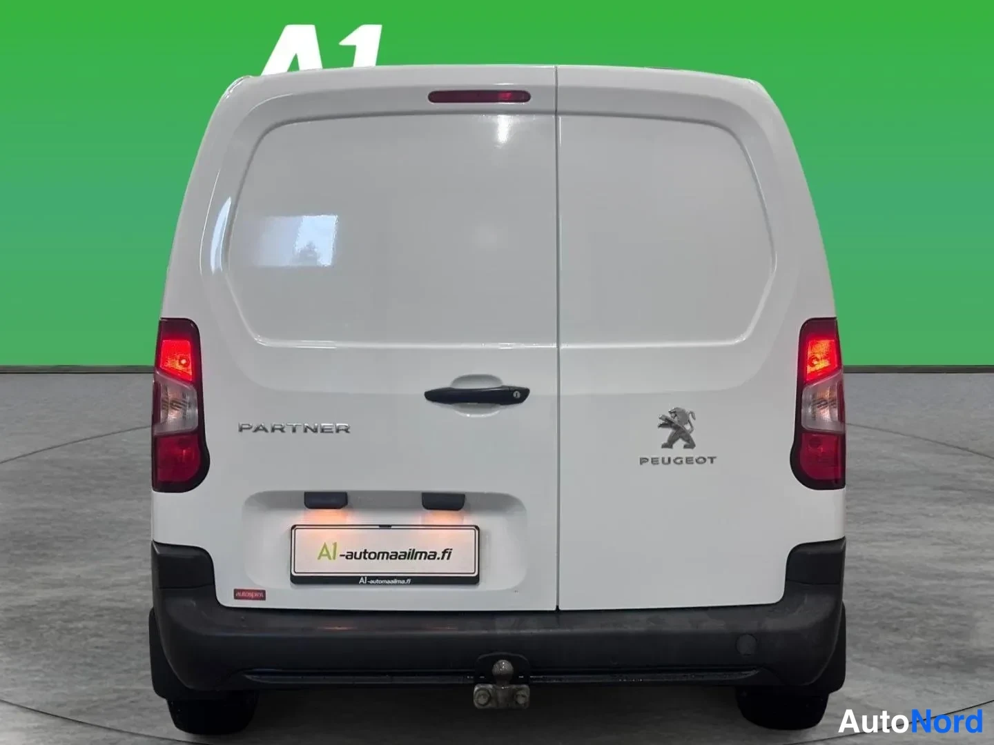 Takaa: Peugeot Partner -pakettiauton takanäky: valkoinen korilevy, takavalot ja Peugeot-tunnus, hinauskoulu takapuskurissa.