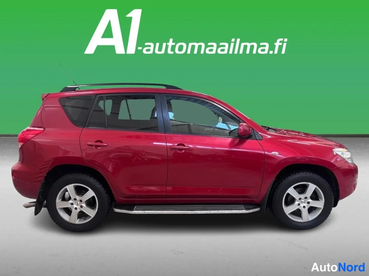 Etuviisto, nokka oikealle: Punaisen Toyota RAV4 -maasturin sivukulma sisätiloissa, vinttikaari, kromilistat ovien alla ja hopeiset kevytmetallivanteet näkyvät.