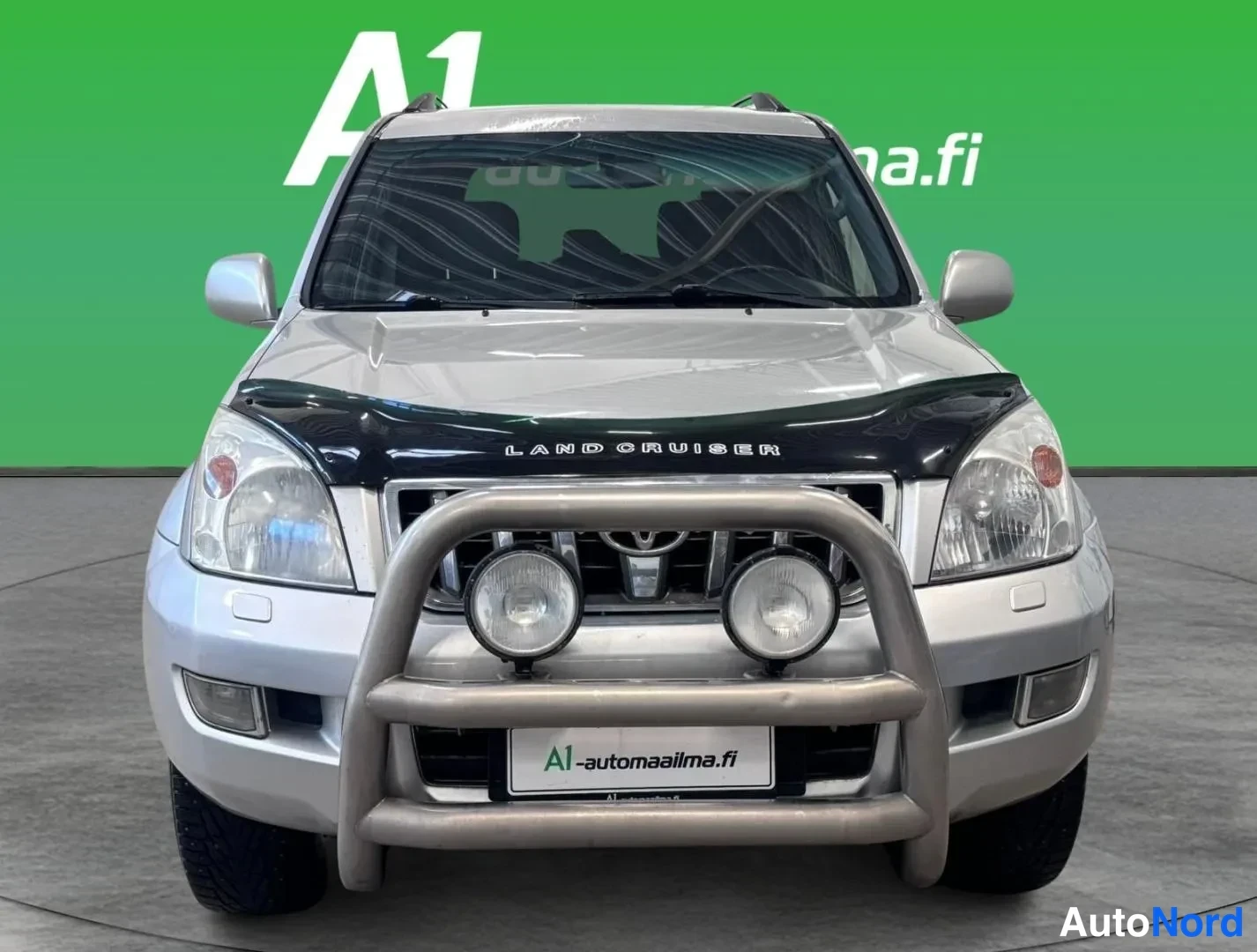 Edestä: Toyota Land Cruiserin keula suoraan edestä kuvattuna; konepellissä LAND CRUISER -teksti, etupuskurissa keulakaari ja lisävalot.
