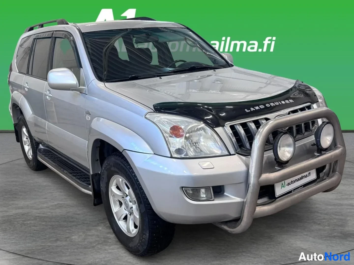 Etuviisto, nokka oikealle: Hopeanvärinen Toyota Land Cruiser kulmassa etuoikealle kuvattuna, peltijalkalistat ovien alla ja keulakaari lisävaloineen.