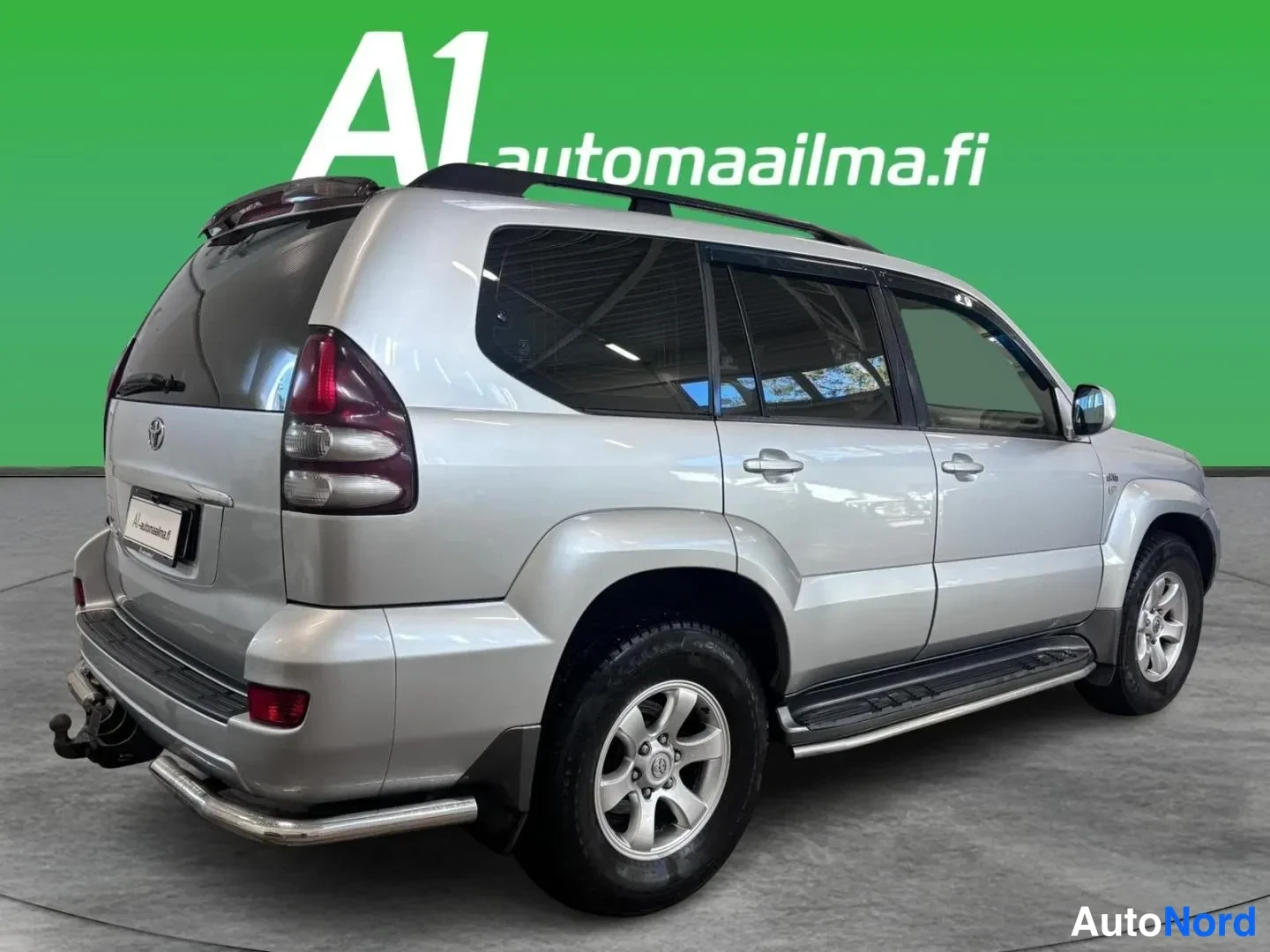 Takaviisto: Hopeanvärinen Toyota Land Cruiser takaviistosta kuvattuna; näkyvät takaosa, kylki, katetut ikkunat, kattotangot ja sivulaitetangot.