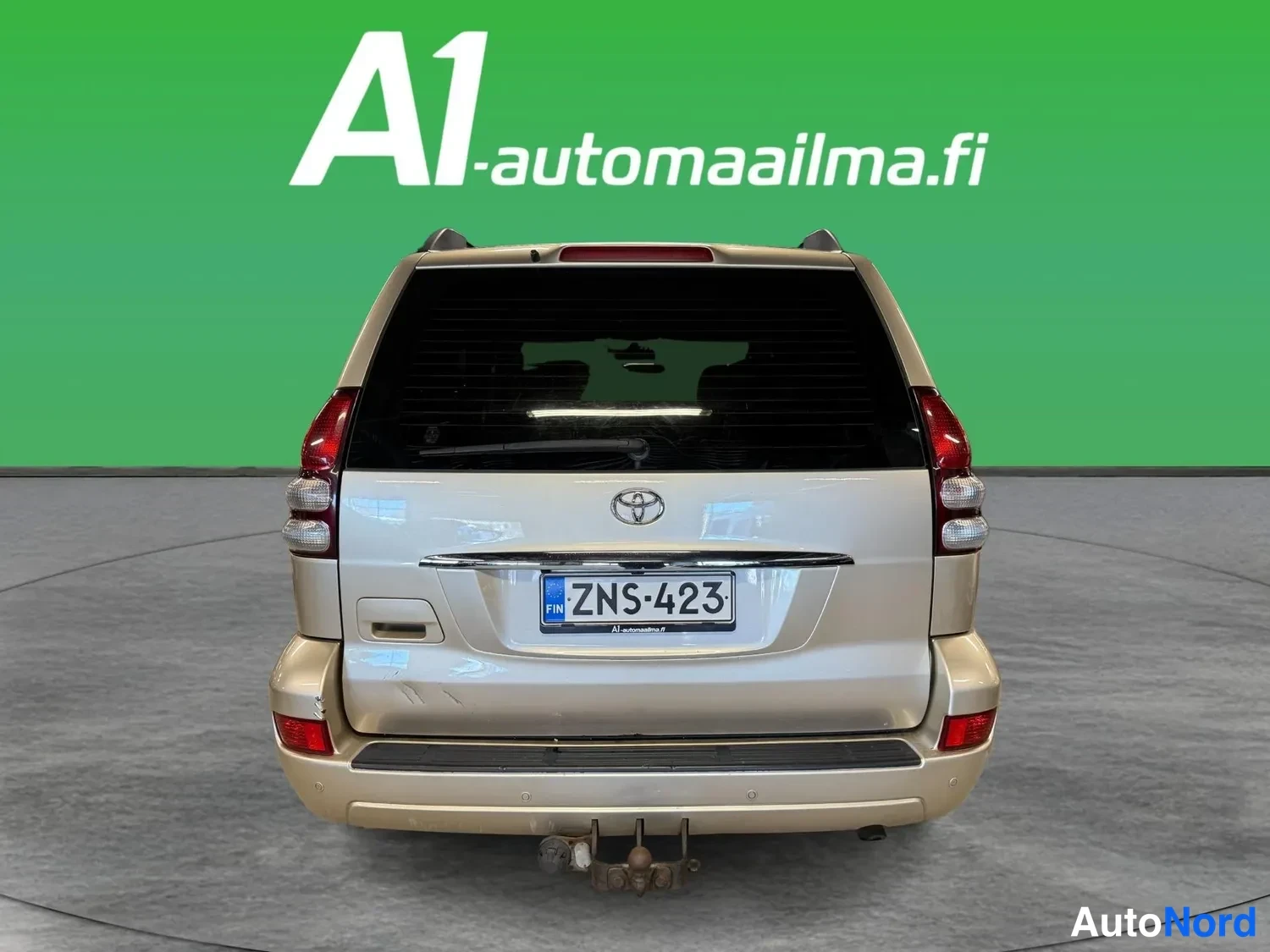 Takaa: Beige Toyota Land Cruiser -urheilumaastopyörän takaosa suoraan takaa, rekisteri, trailerikoukku näkyvissä puskurin alla.