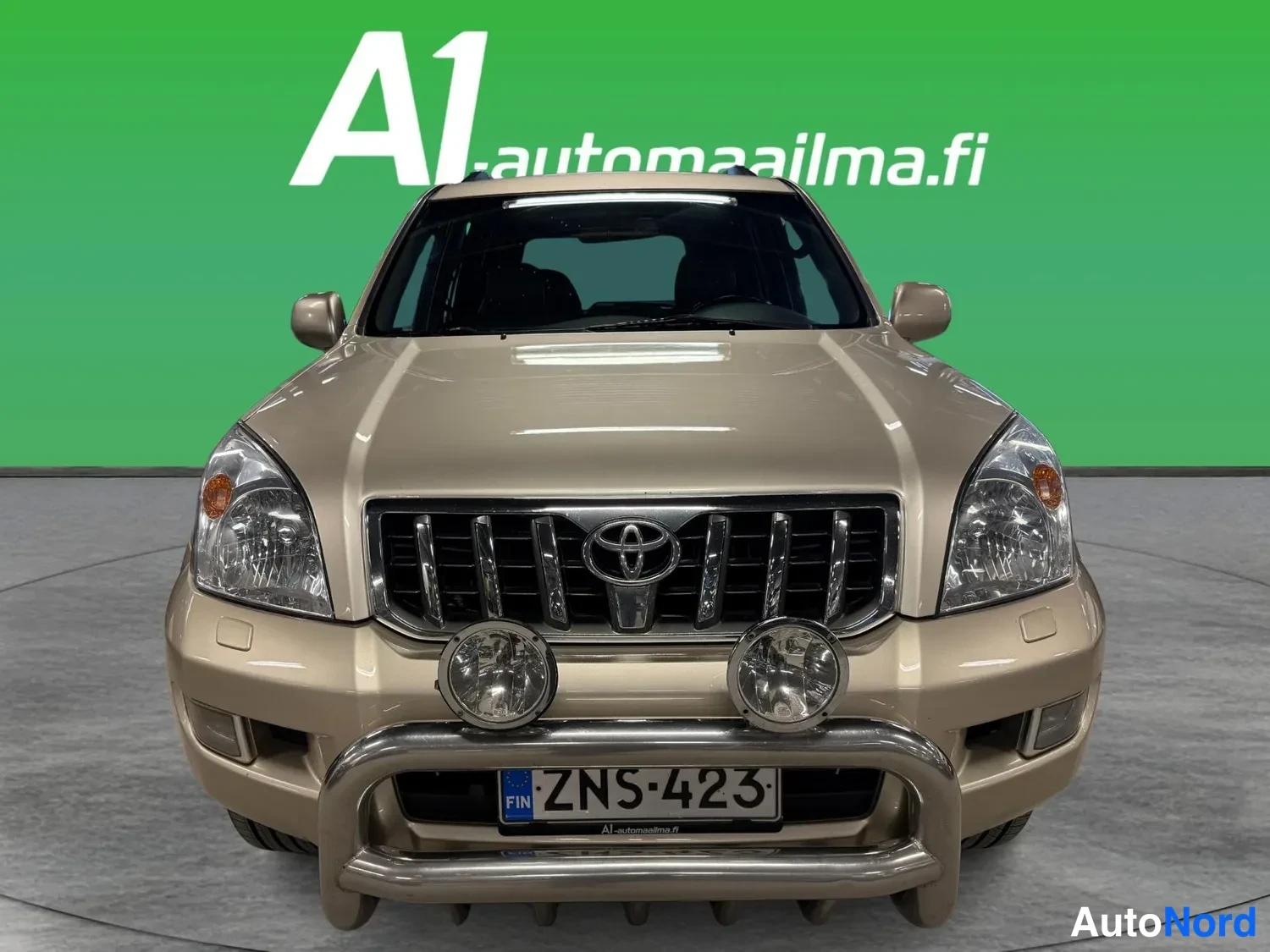 Edestä: Toyotan etunäkymä: beige koriväri, kromikehys etupuskurissa ja kaksi lisävaloa, rekisteri.