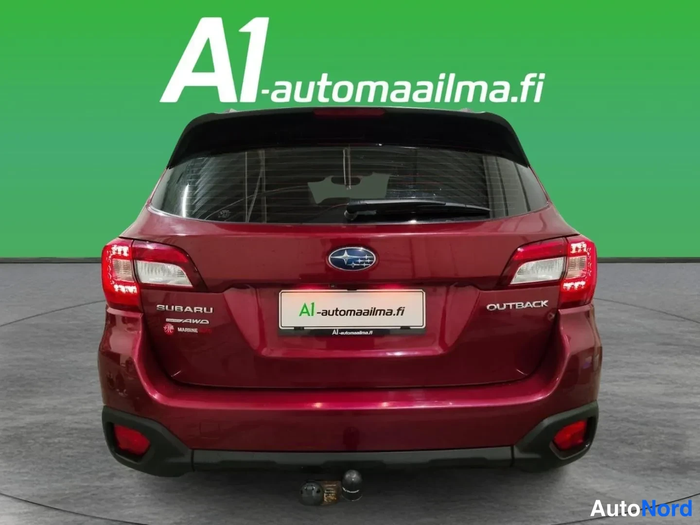 Takaa: Auton takaosa suoraan takaa: tummanpunainen farmariauto, SUBARU-, AWD- ja OUTBACK-tekstit takaluukussa, punaiset takavalot ja vetokoukku puskurin alla.