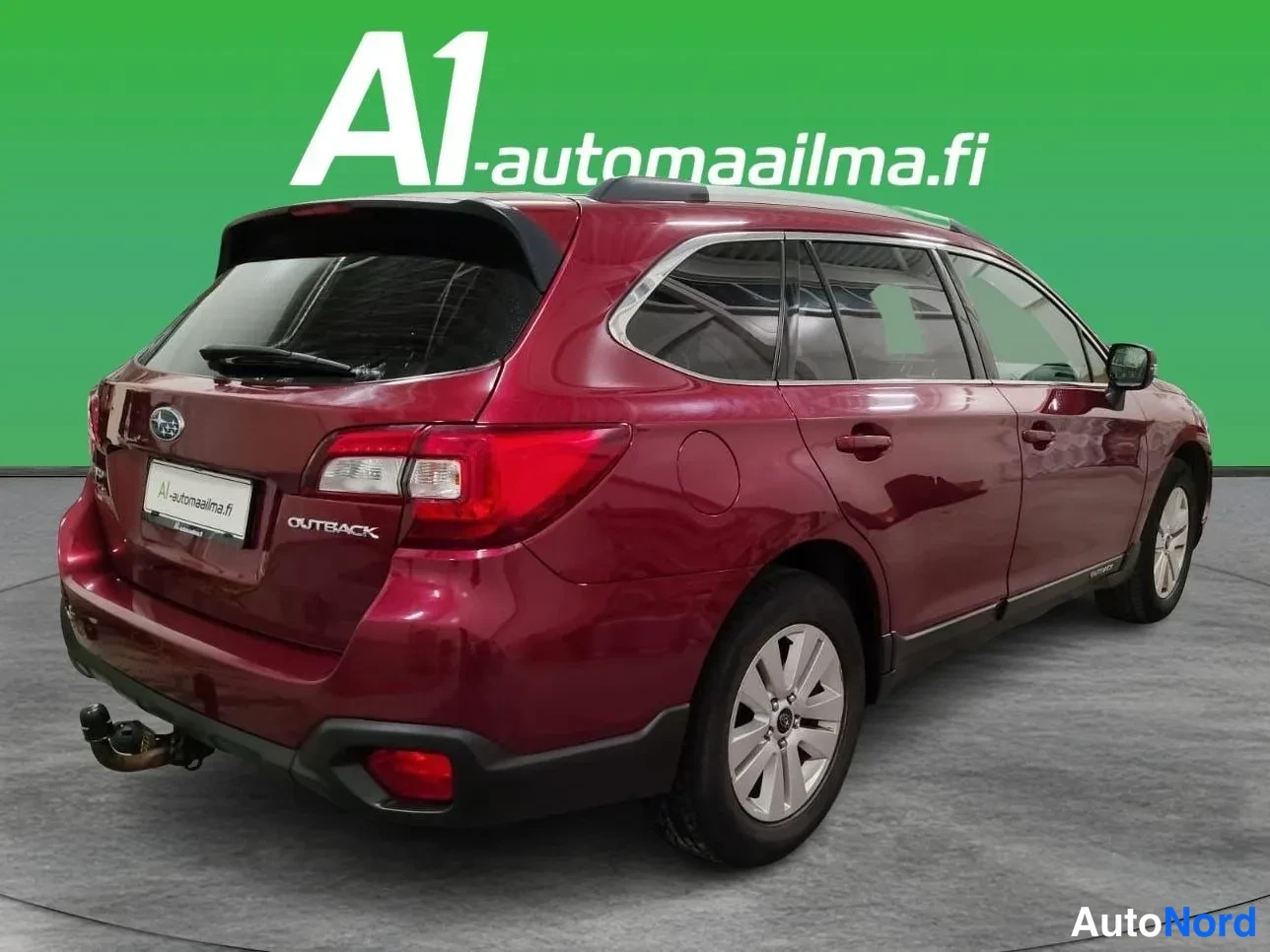 Takaviisto: Auton takaosa ja vasen kylki kulmasta: tummanpunainen farmari, katukäyttö, kattokaiteet, OUTBACK-teksti takaluukussa ja vetokoukku.
