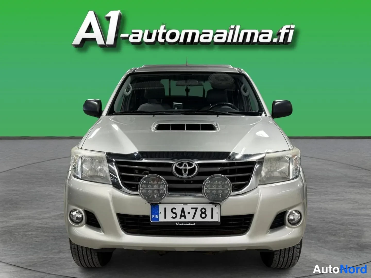 Edestä: Hopeanvärinen pickup suoraan edestä; rekisteritunnus, lisävalot etupuskurissa.