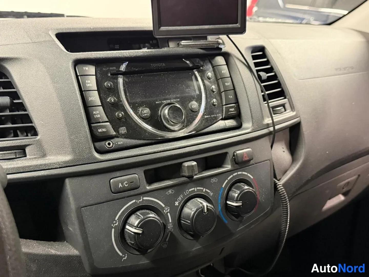 Sivulta: Kojeiston keskiosan lahikuva: Toyota-merkkinen radio-CD-soitin ja A/C-nappi kolmella sahkomahdilla.