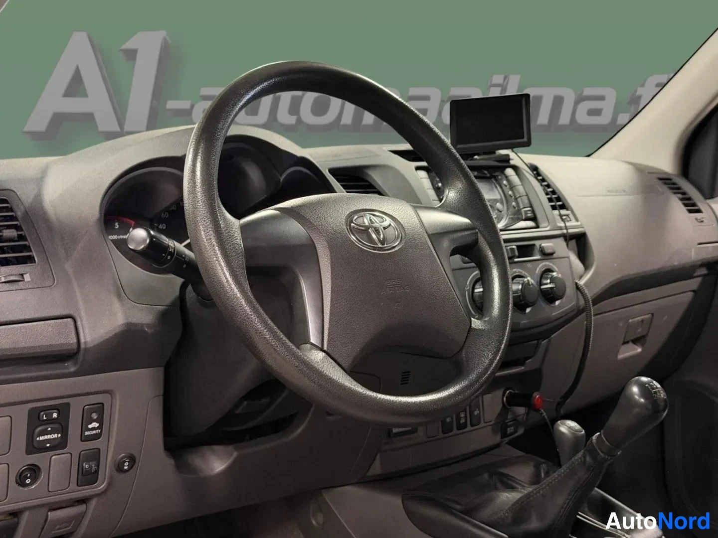 Muu: Ohjauspyörä Toyota-embleemillä ja mittaristo, taustalla törmäystunnistin ja radiovarusteet, mikä kertoo ajosuunnasta.