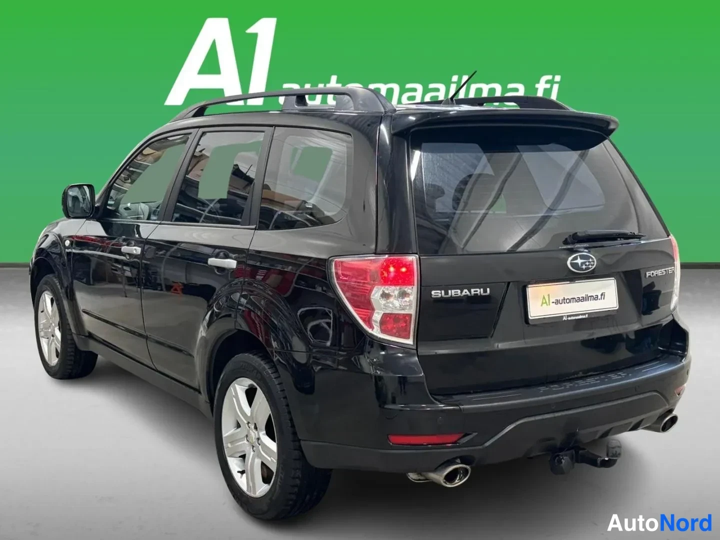 Takaviisto: Mustan Subaru Foresterin takakulmanäkyväscreenshot: takavalot, SUBARU-merkintä, katetut kattokaiteet ja perävaunu-kytkin näkyvät.