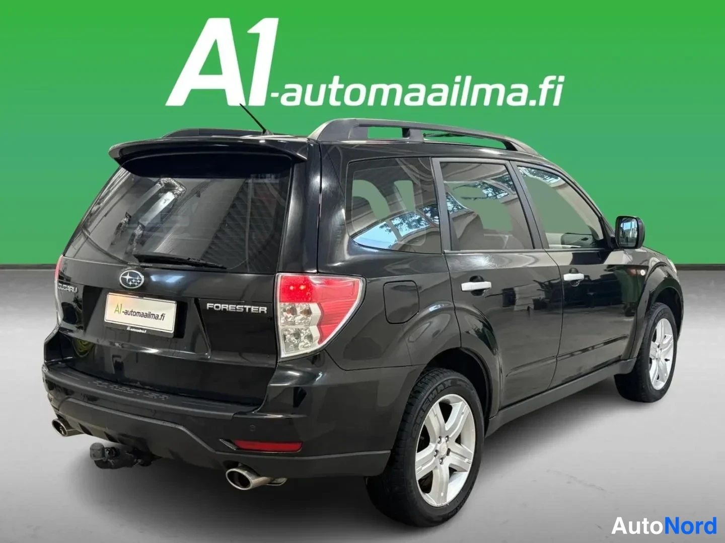Takaviisto: Mustan Subaru Foresterin takakulmanäkyväscreenshot oikealta: takapaneeli FORESTER-tekstillä, kattokaiteet ja hopeiset vanteet näkyvät.