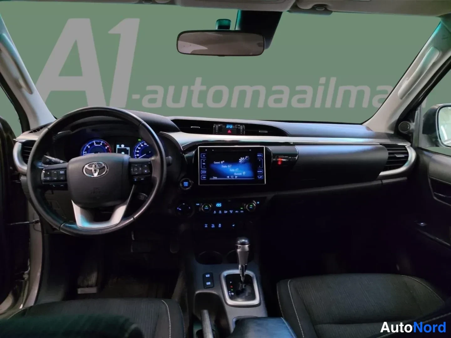 Etuviisto, nokka oikealle: Auton sisätilat: ohjauspyörä Toyota-logolla, mittaristo, kosketusnäytöllinen radio ja automaattivaihteiston valitsin keskikonsolissa.