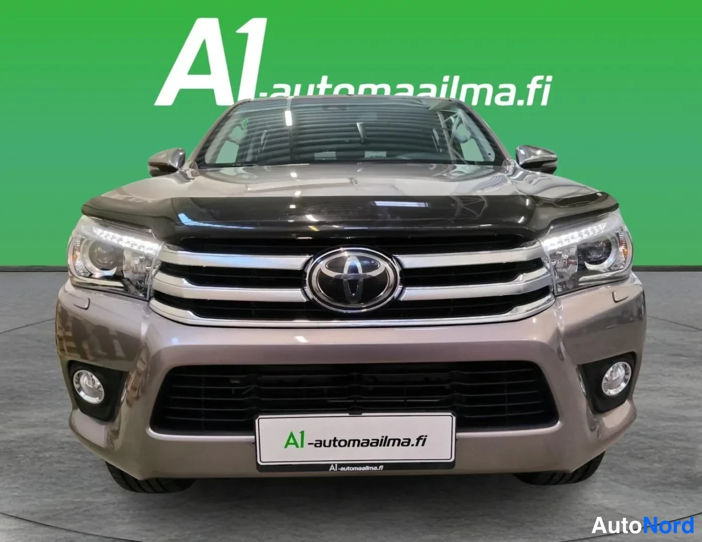 Edestä: Toyota Hiluxin suora etukuva, jossa näkyvät kromilamaanit, Toyota-merkki, LED-päiväajovalot ja sumuvalot.