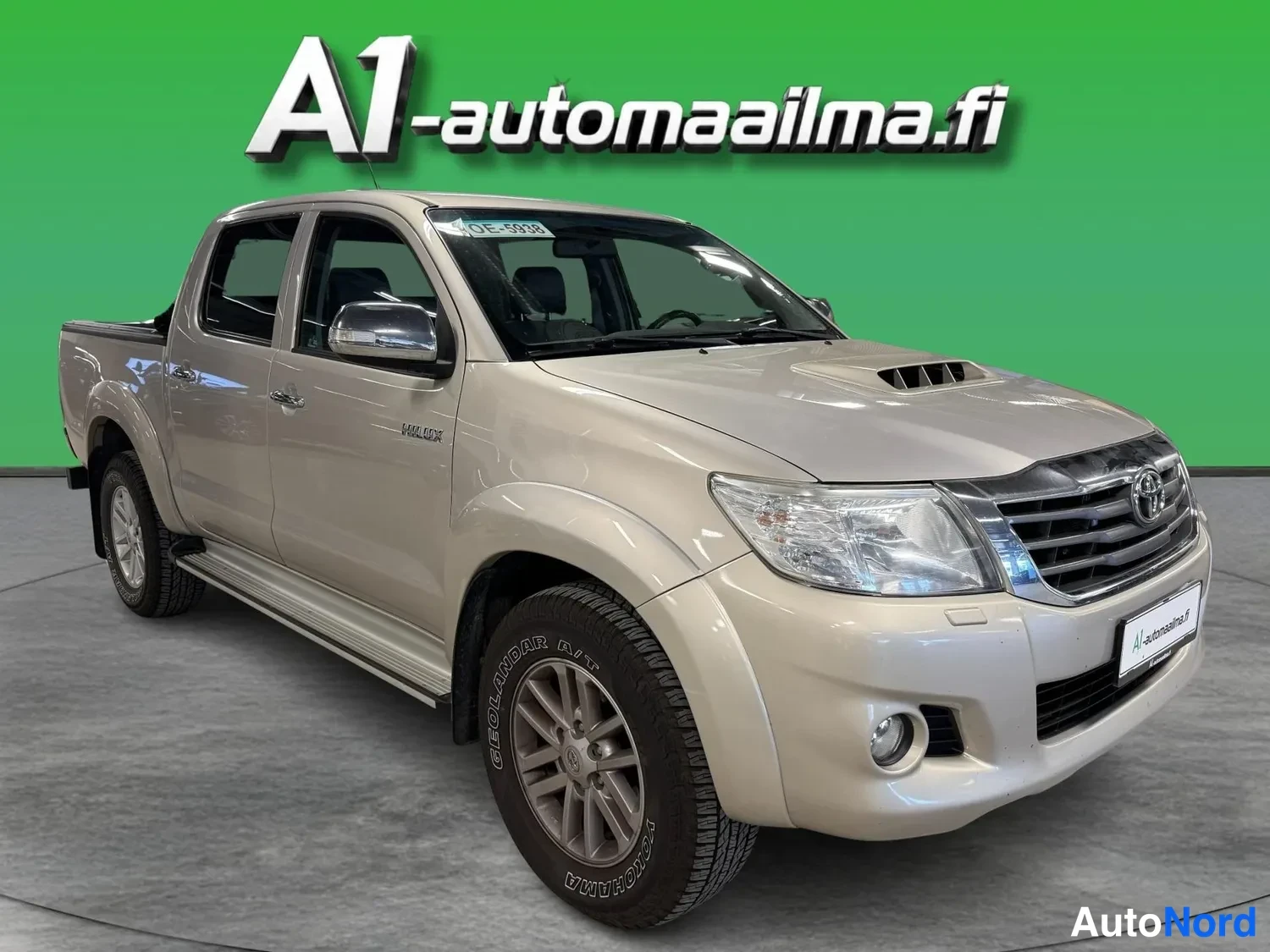 Etuviisto, nokka oikealle: Beige Toyota Hilux Double Cab -malli kulmassa kuvattuna nokka oikealle, keulan ja vasemman sivun näkyessä.